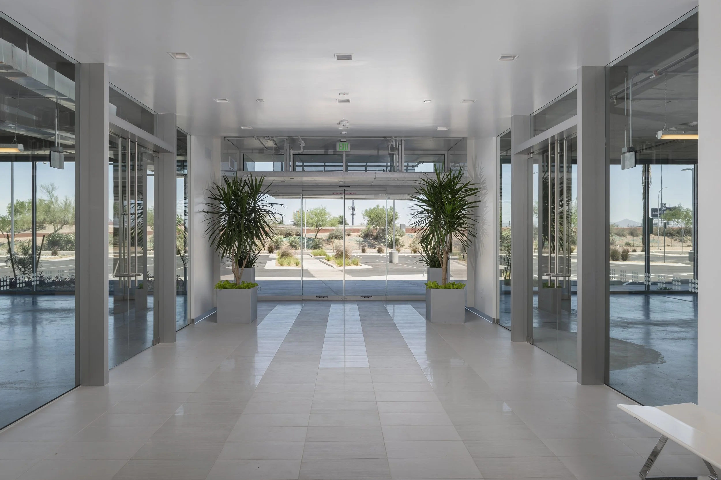 Modern building lobby with glass doors, potted plants, and natural light.