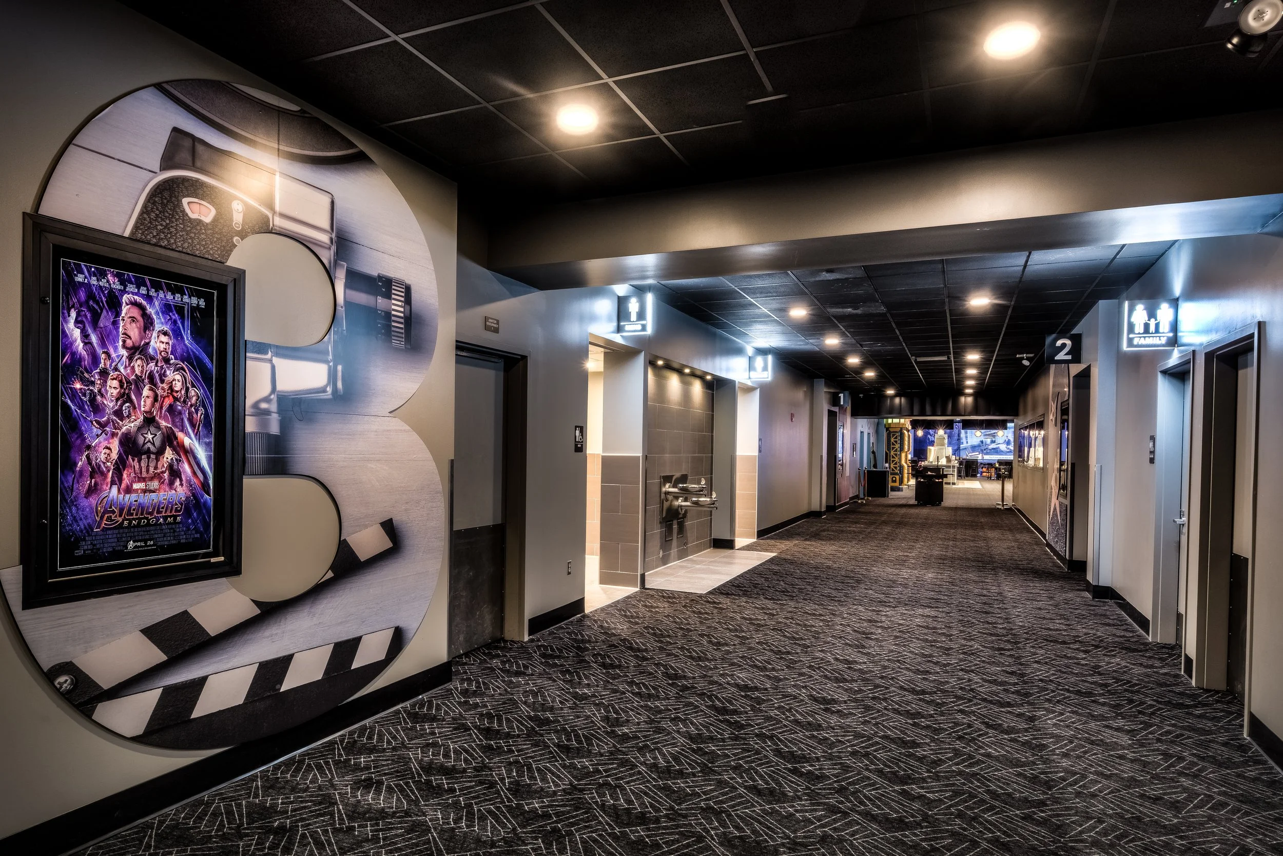Movie theater hallway with elevators, illuminated exit signs, and a poster for Avengers: Endgame.