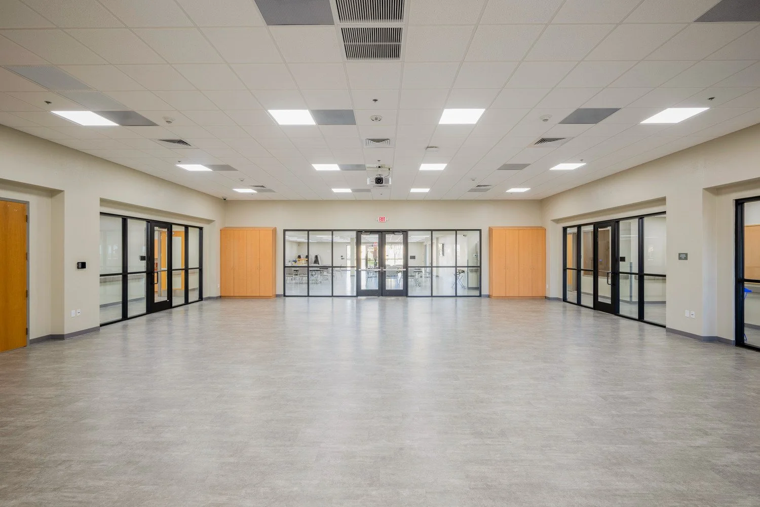 Empty classroom with glass walls and wooden cabinets, ceiling lights, and gray flooring.