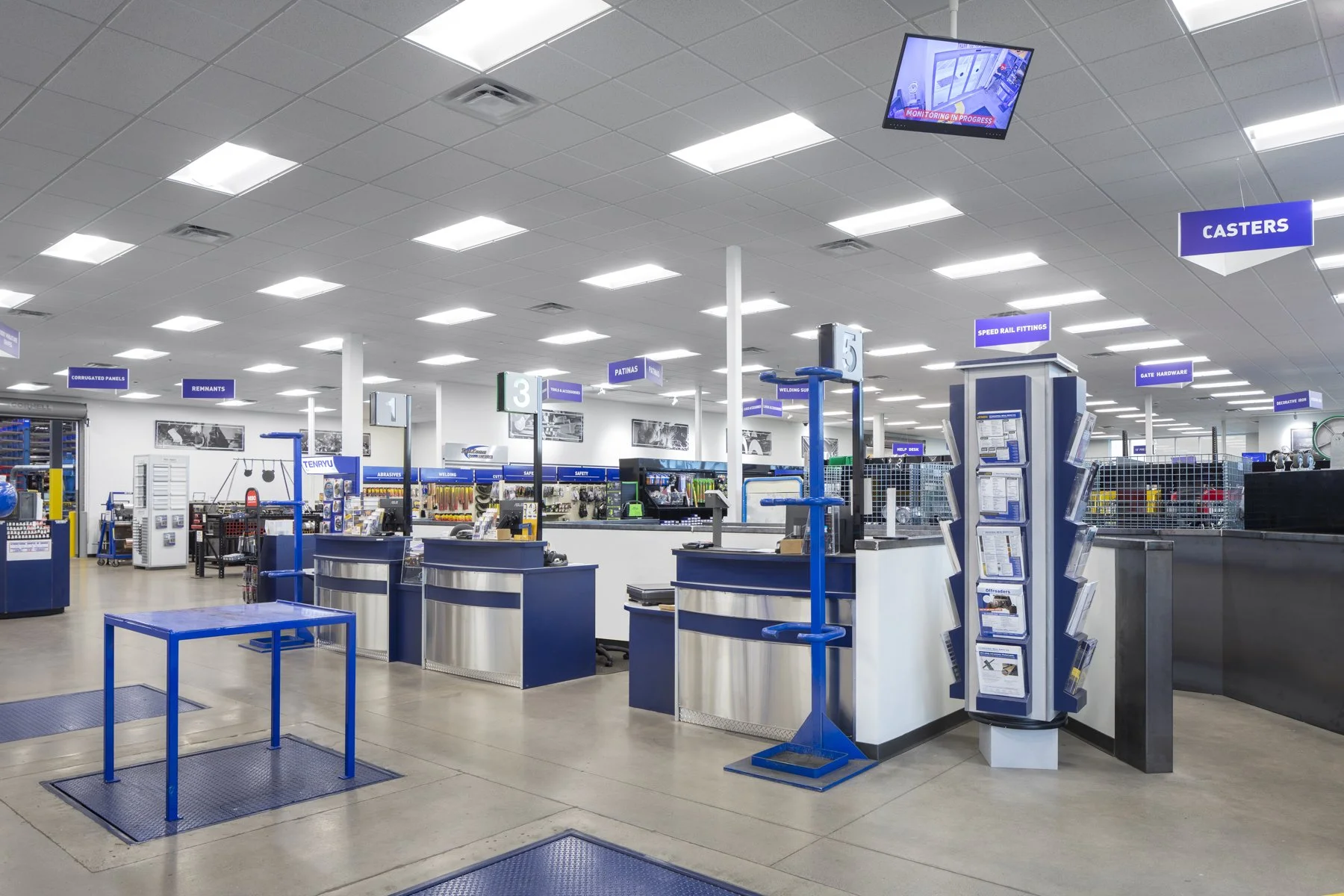 Interior of a hardware store with checkouts, blue signage hanging from the ceiling, and various hardware supplies on shelves.