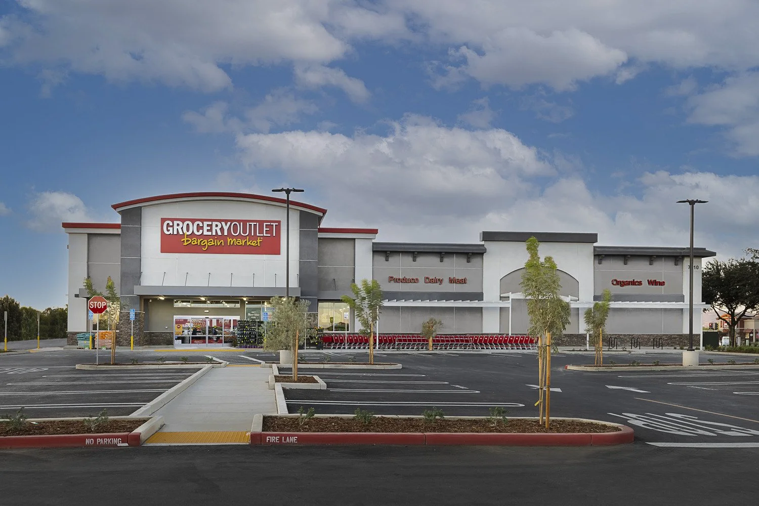 Empty parking lot in front of a grocery store with signs reading Grocery Outlet, Bargain Market, Produce, Dairy, Meat, Organics, Wine, and a stop sign near the entrance.