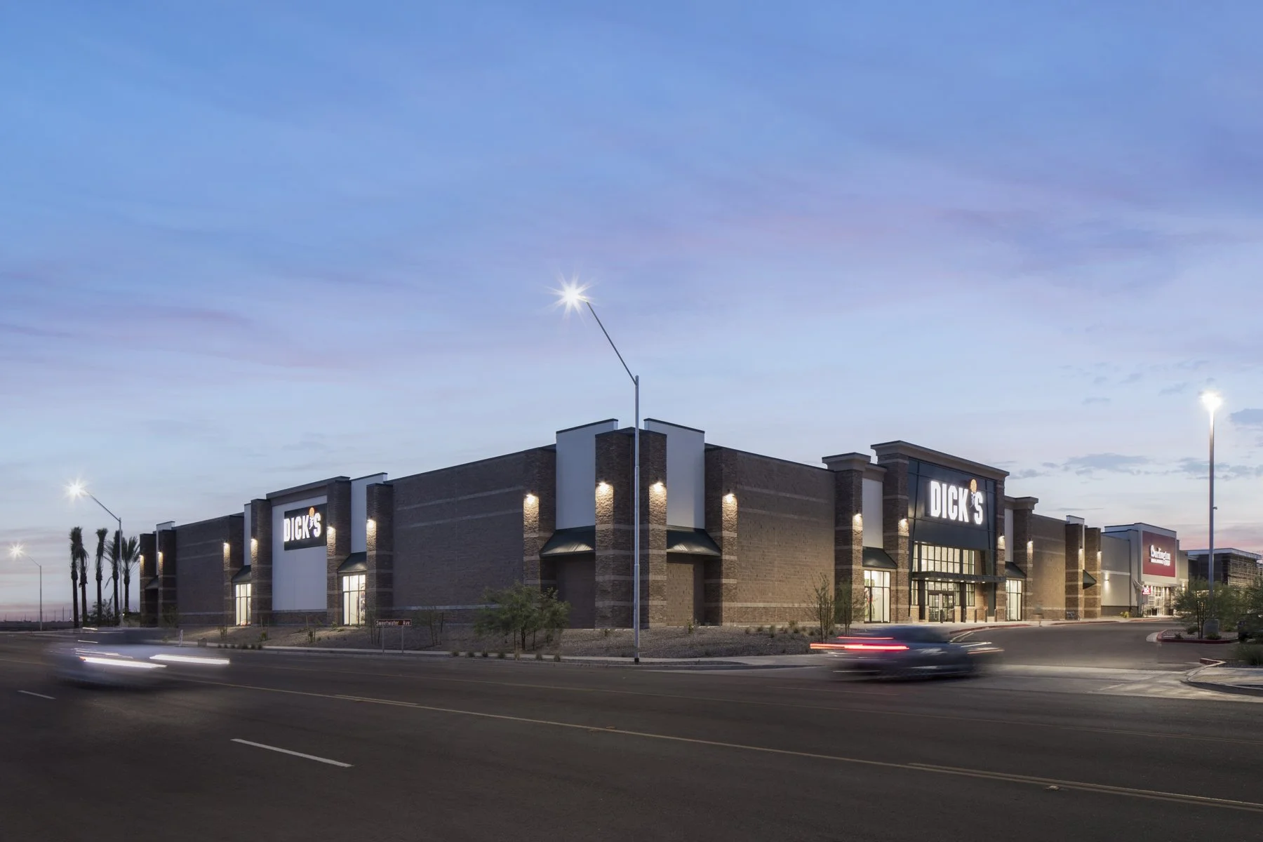 A large retail store building named Dick's Sporting Goods at dusk, with illuminated signs and parking lot in the foreground.
