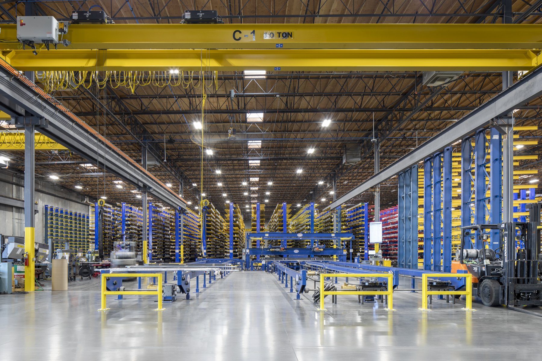 Interior of a large warehouse or manufacturing facility with shelving, machinery, and a forklift on the right side.