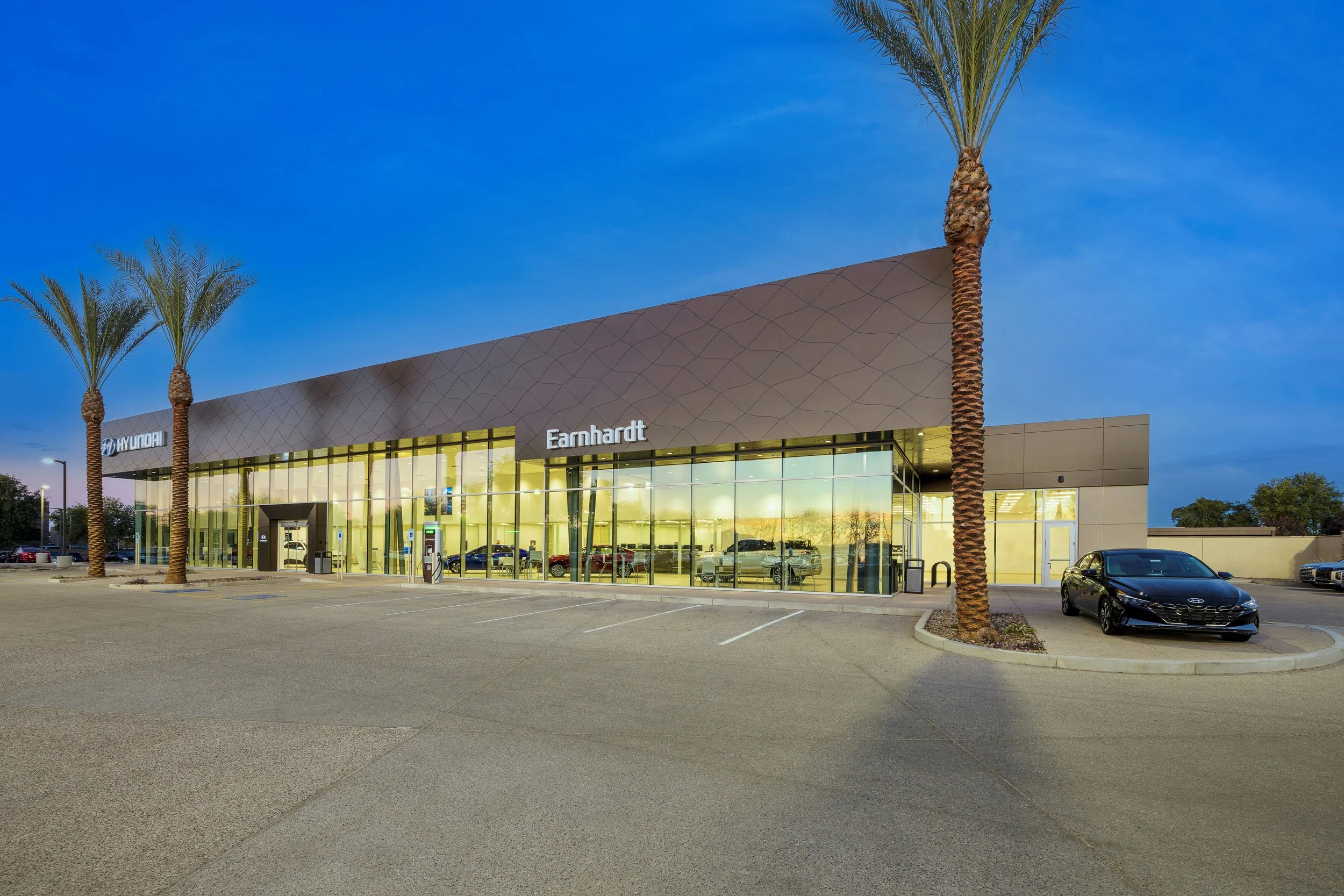 Car dealership building with glass front and palm trees in the parking lot at dusk, with the signs reads 'Earnhardt' and 'Hyundai'.