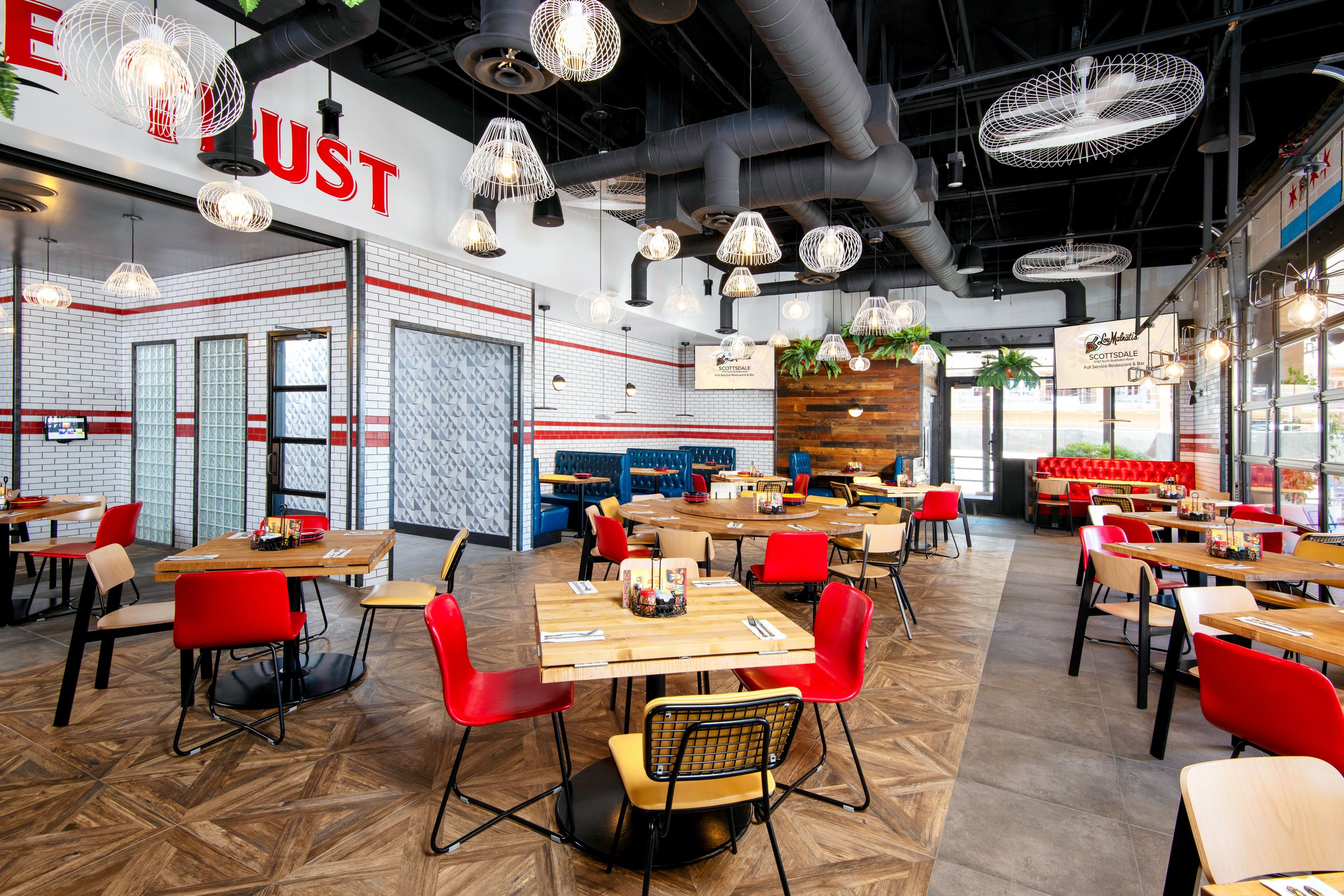 Empty modern restaurant dining area with wooden tables, red and beige chairs, hanging light fixtures, and large windows.
