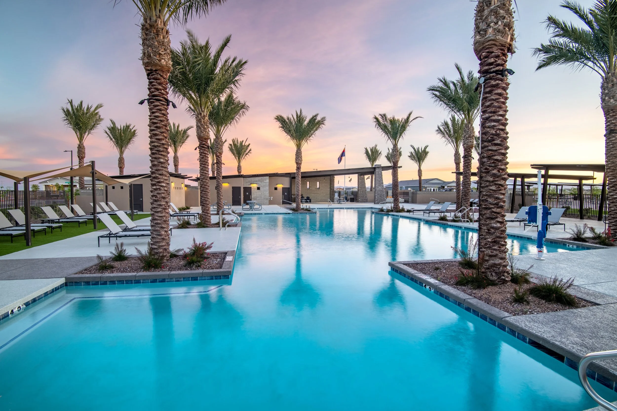 Palm trees surrounding a swimming pool at sunset with lounge chairs and a flag in the background.