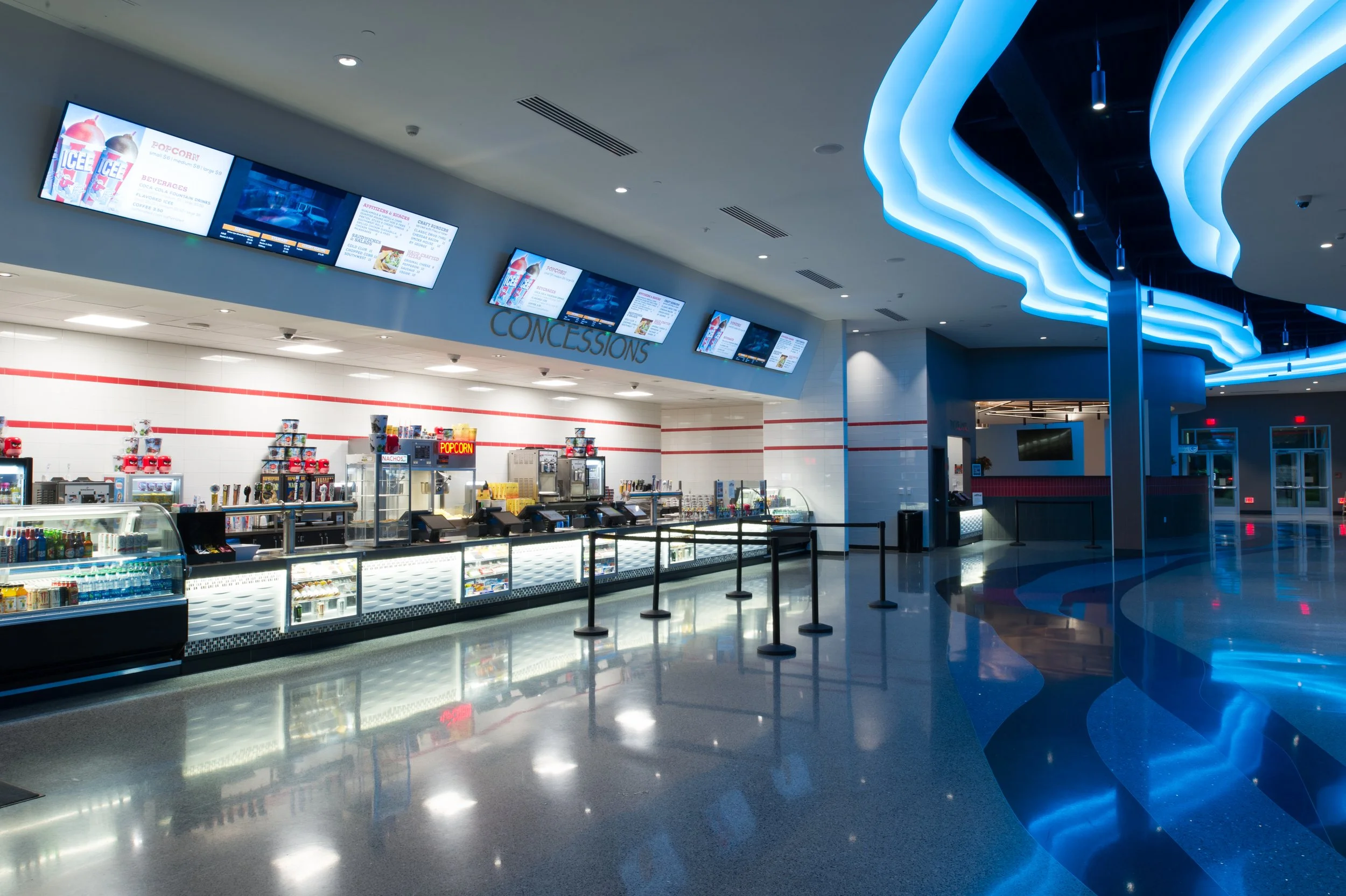 Movie theater concession stand with digital menu screens and blue ceiling lighting.