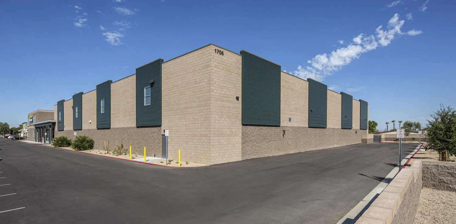 Exterior view of a beige commercial building with a parking lot, under a partly cloudy blue sky.