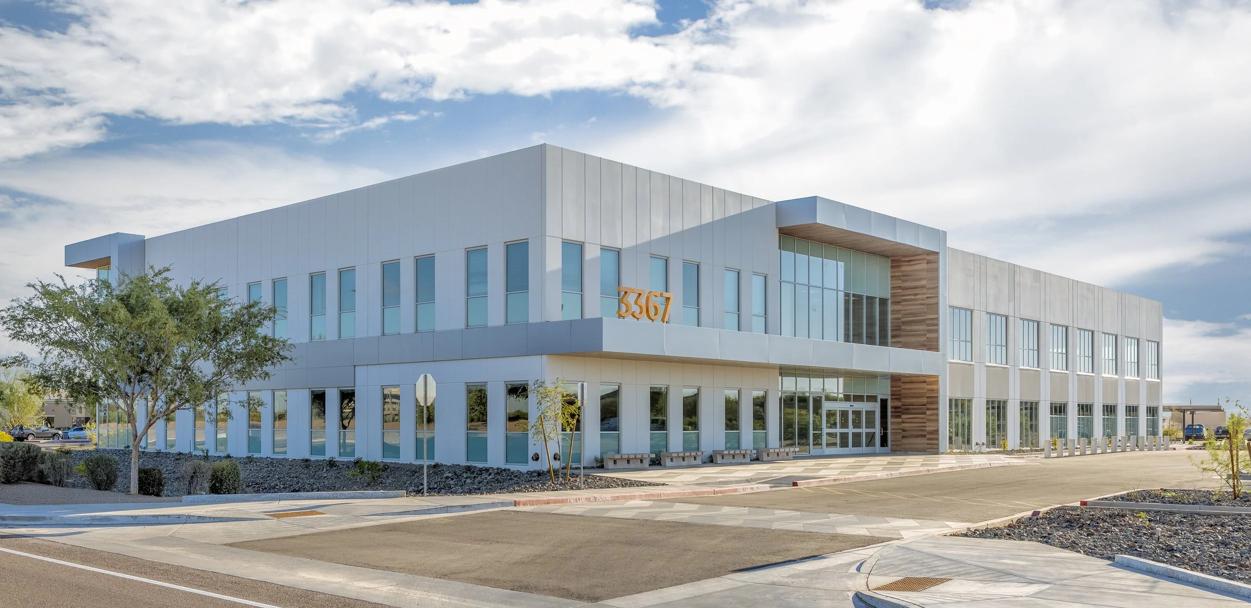 Modern three-story office building with large glass windows, beige and wood exterior panels, and the number 3367 displayed in orange above the entrance.