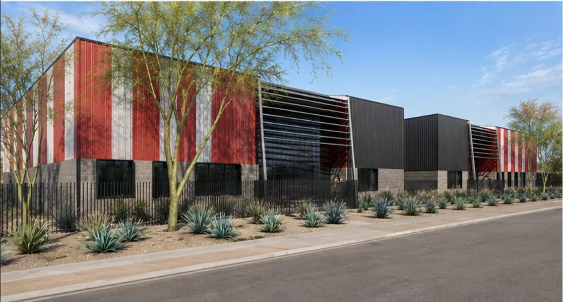 Modern commercial building with red, black, and gray exterior, surrounded by desert landscaping and trees, along a street with a clear blue sky.