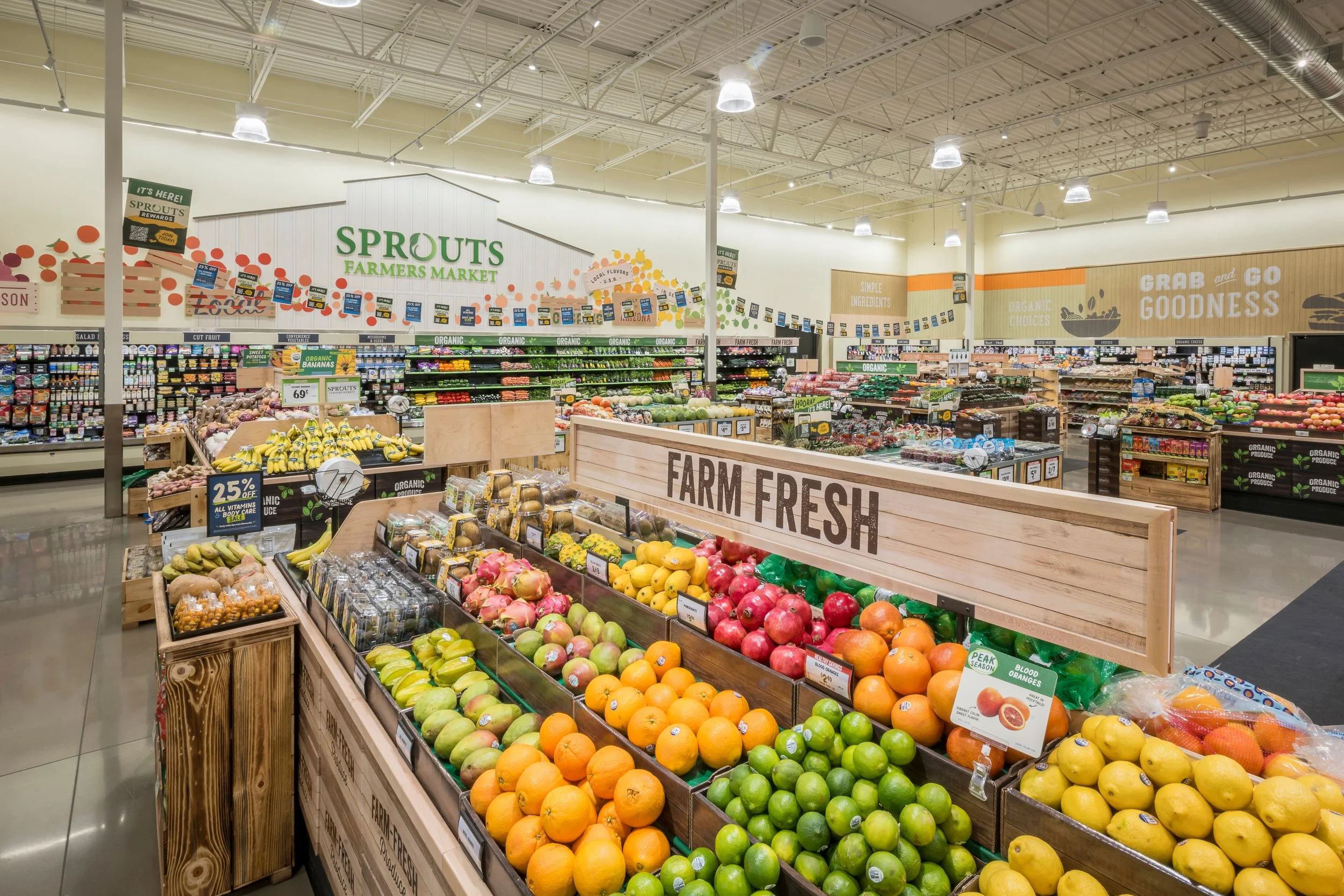 Produce section at Sprouts Farmers Market with fresh fruits like oranges, lemons, limes, and apples on display, and a large sign reading 'Farm Fresh' in the foreground.