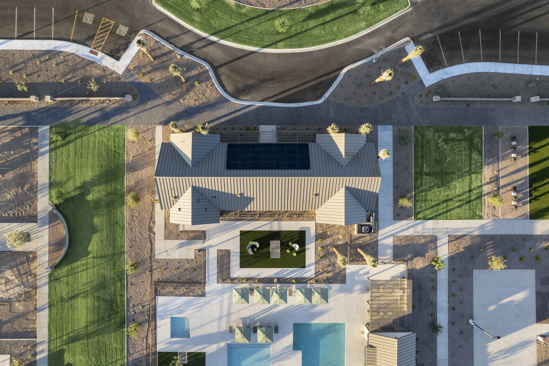 Aerial view of a modern community area with a building, a small playground, a swimming pool, and landscaped green spaces with trees and pathways.