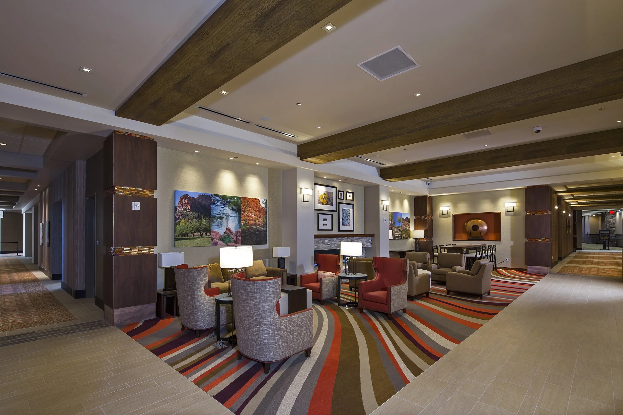 Hotel lobby with comfortable seating, colorful carpet, framed artwork on the walls, and warm ambient lighting.