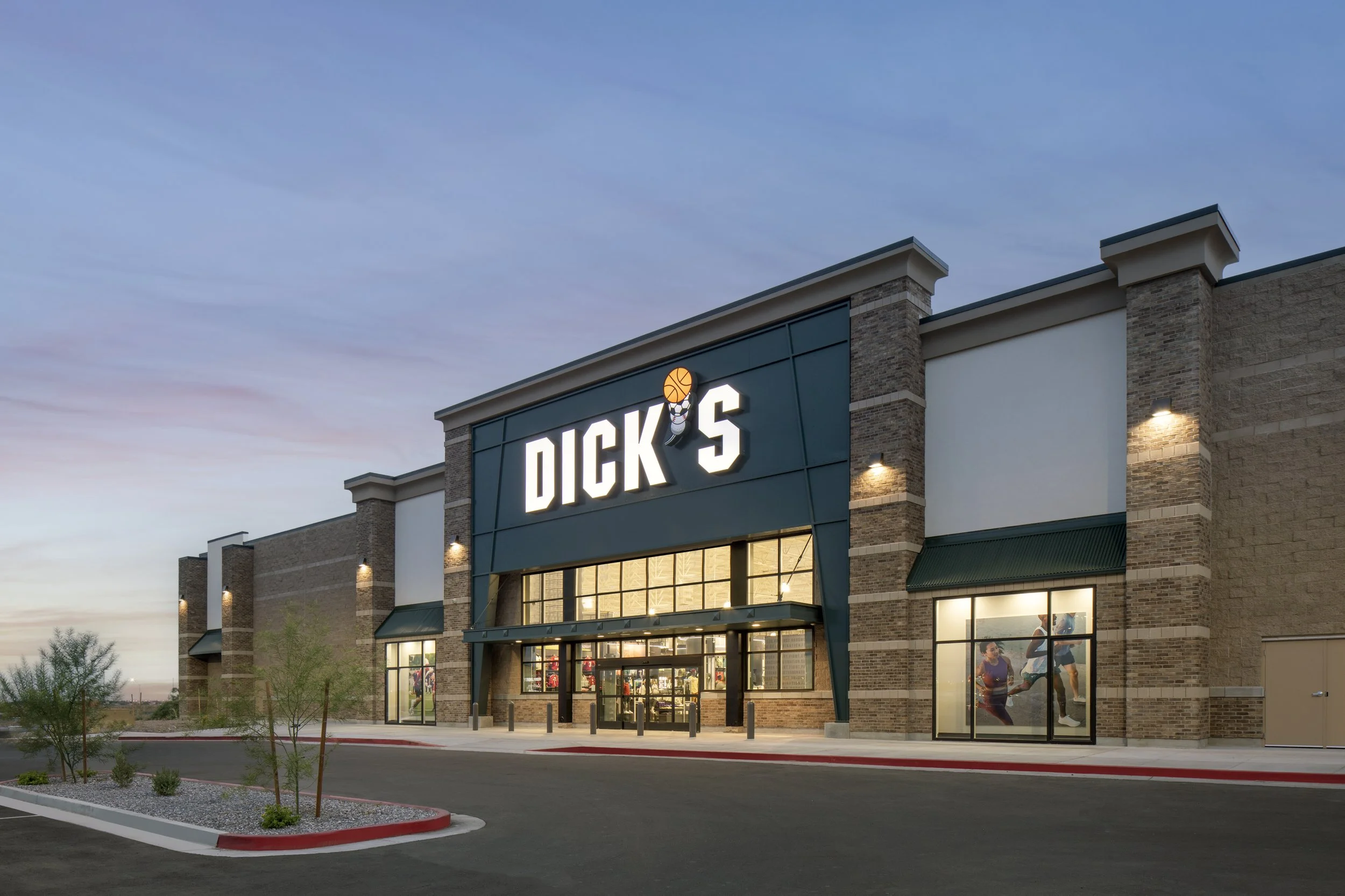 Exterior view of a Dick's sporting goods store during dusk with illuminated sign and glass doors.
