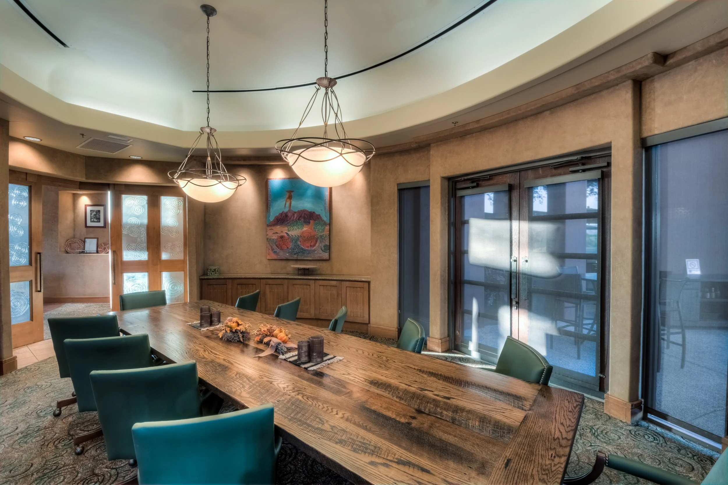 Empty conference room with a large wooden table, green chairs, sliding glass doors, and a painting on the wall