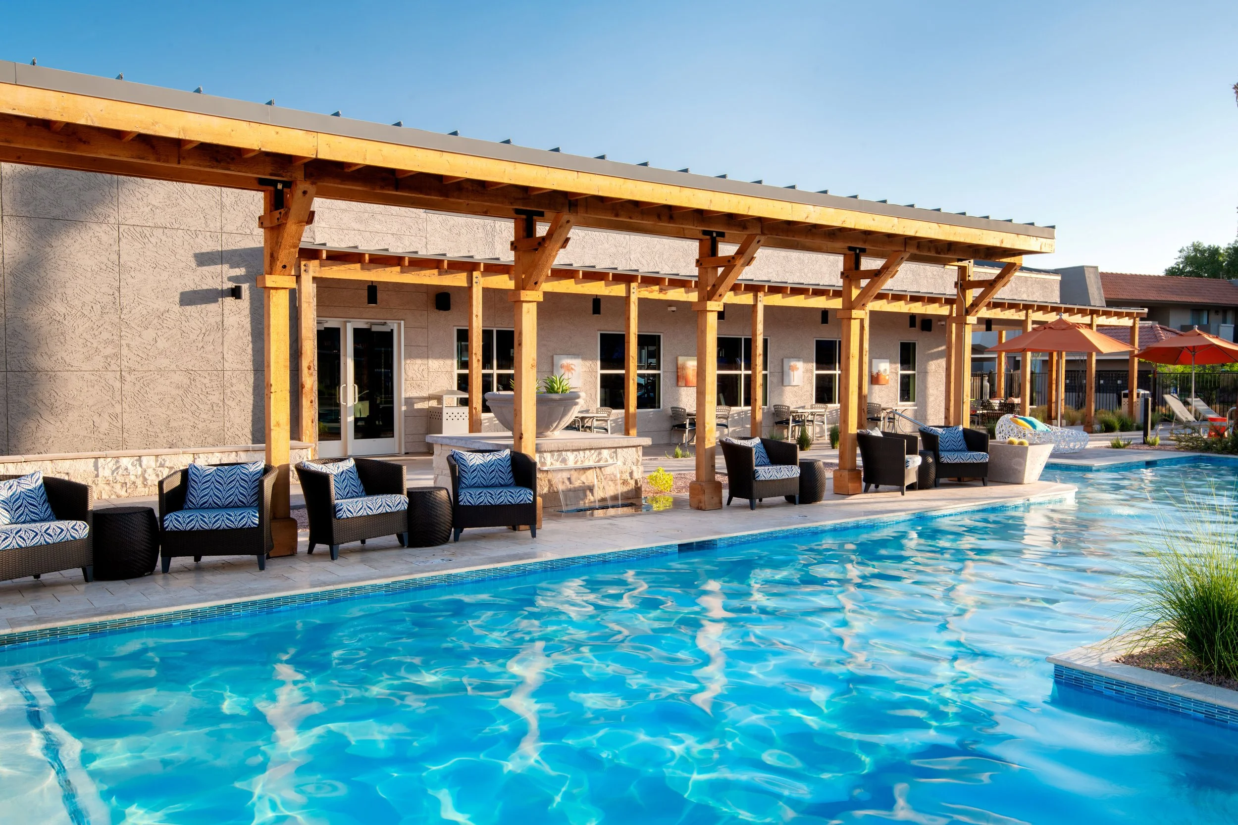 Swimming pool with lounge chairs and outdoor seating area under a wooden pergola, sunny day.