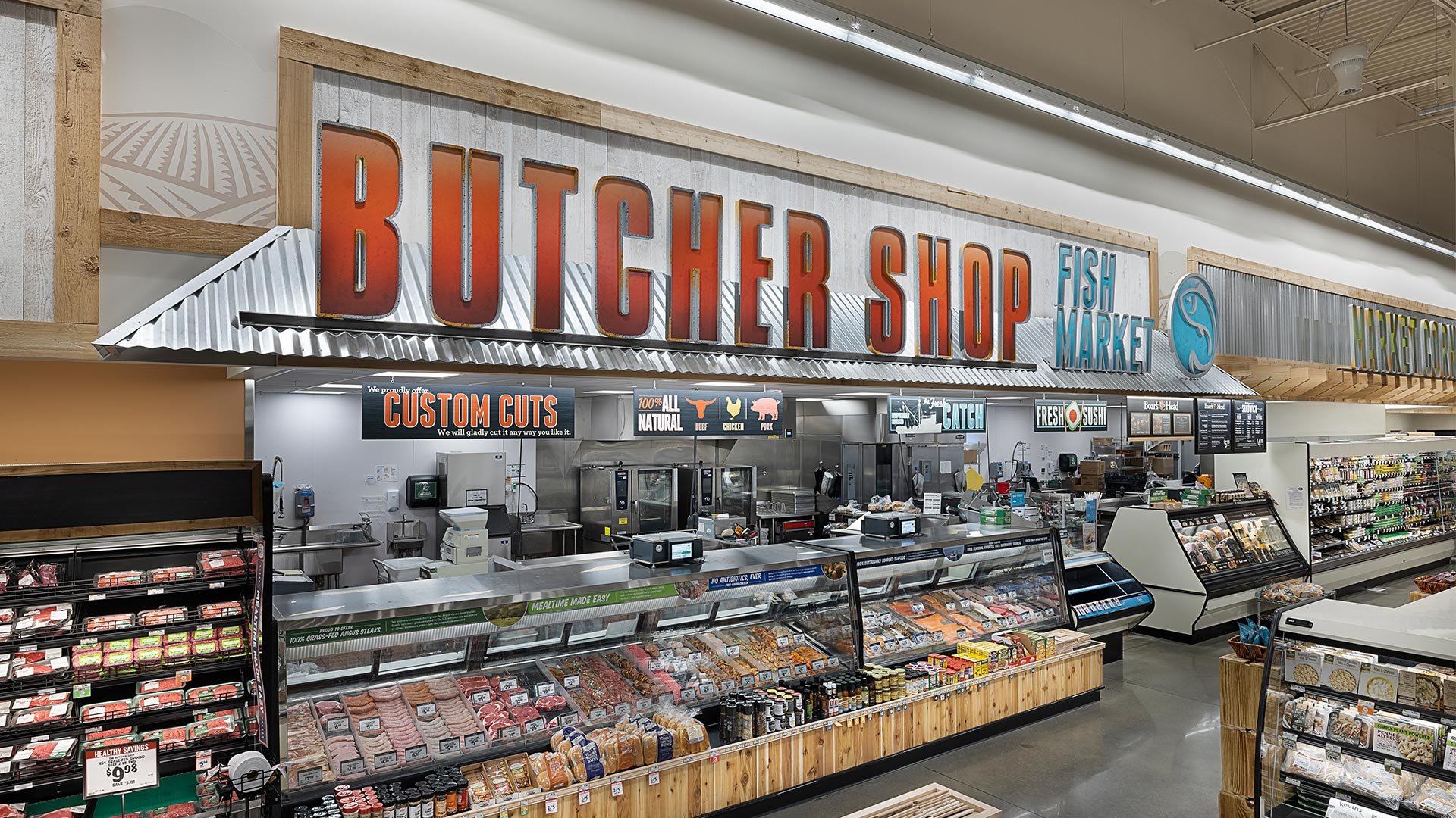 Inside a butcher shop at a fish market area with meat and seafood displays, including signs for custom cuts, and a counter with various packages of meat.