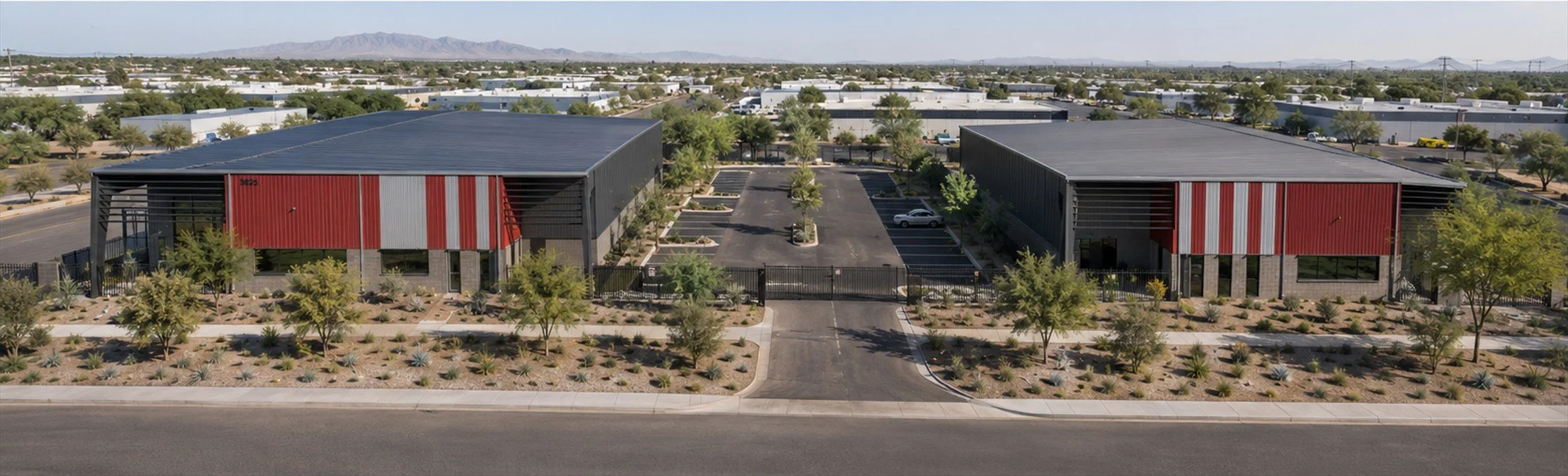 Aerial view of a business complex with two large buildings, parking lot, trees, and desert landscaping in a suburban area.
