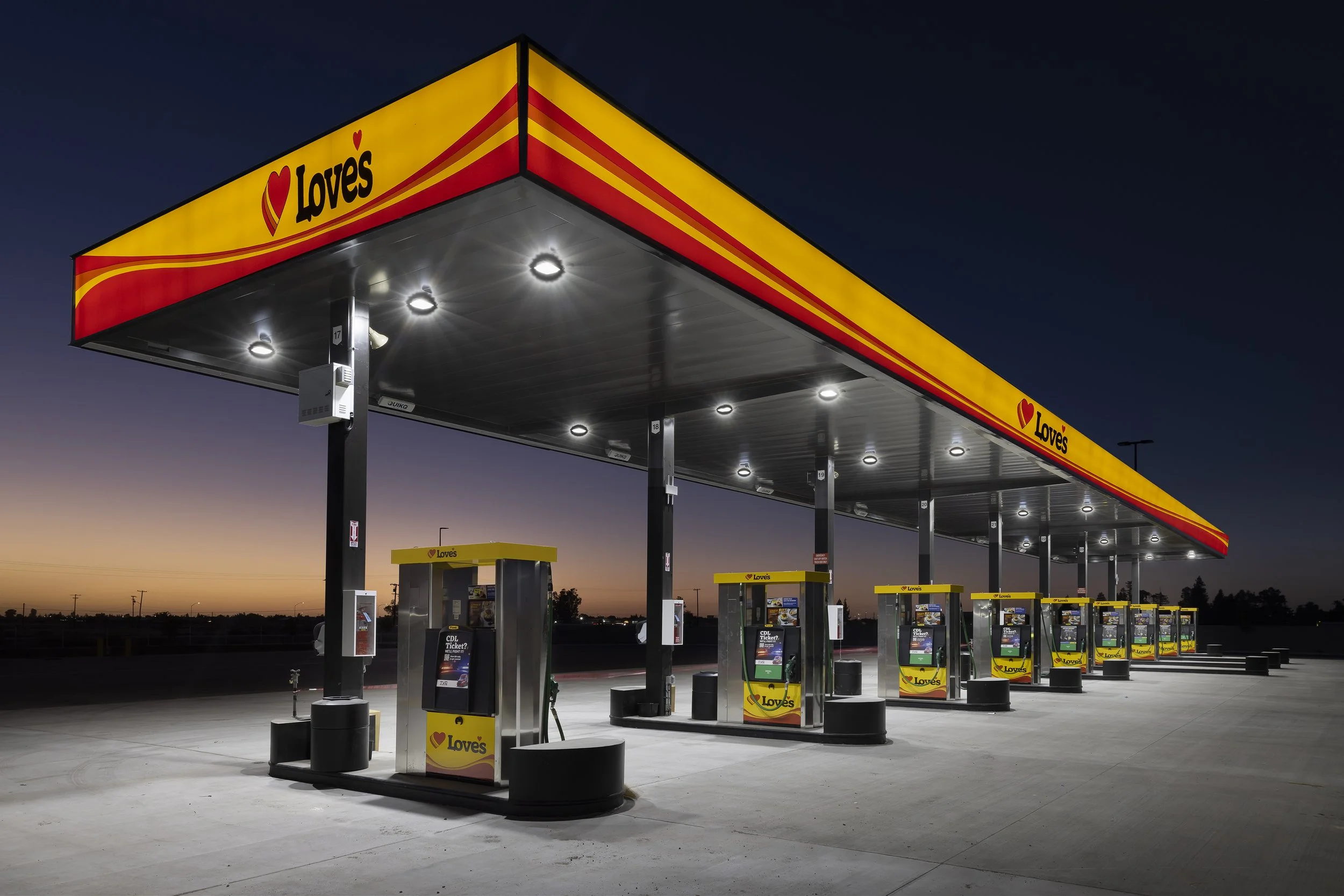 Empty Love's gas station at dusk with illuminated pumps and canopy, featuring yellow and red branding.