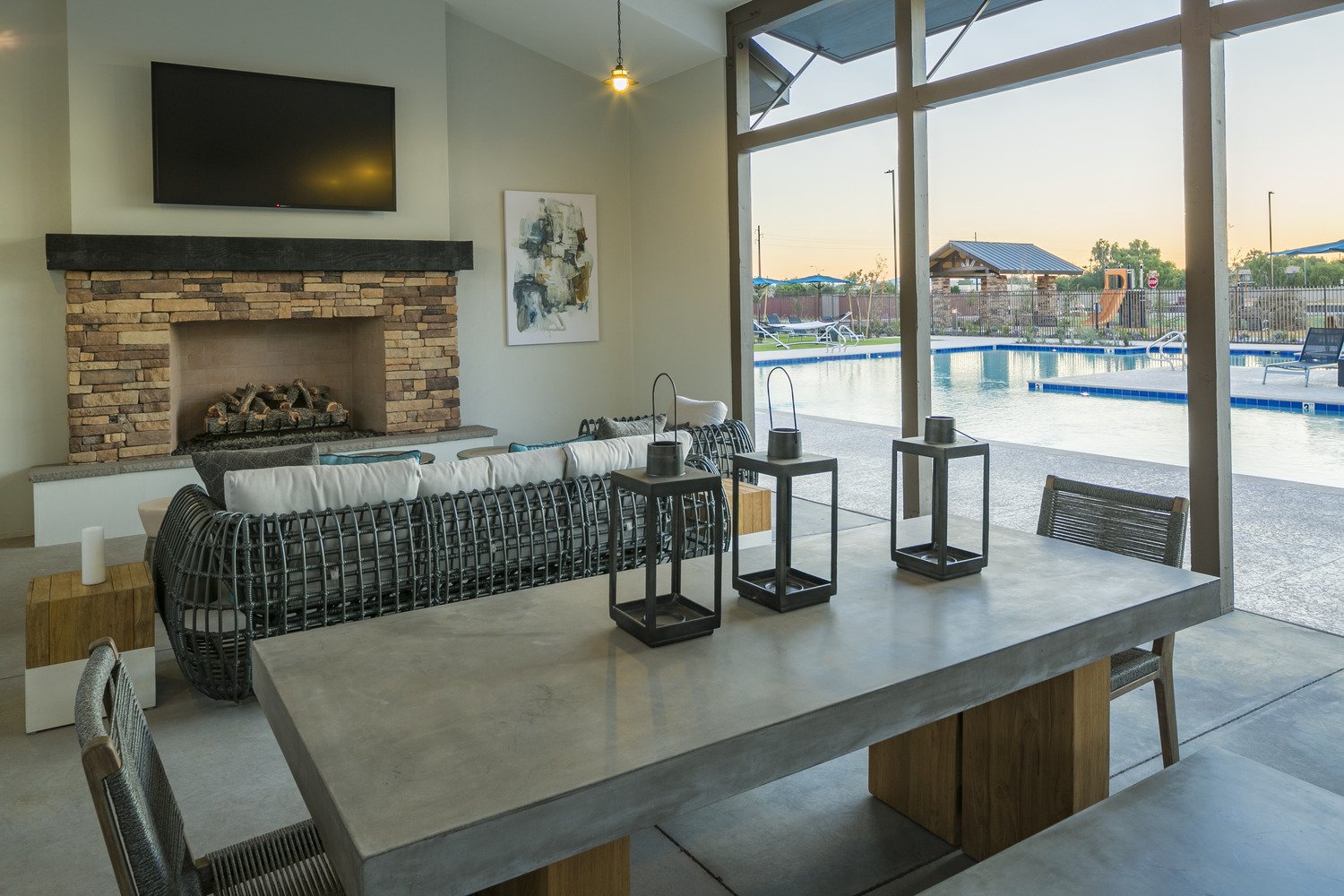 Indoor lounge area with a fireplace, a mounted TV, a large abstract painting, and a view of a swimming pool outside through large windows.