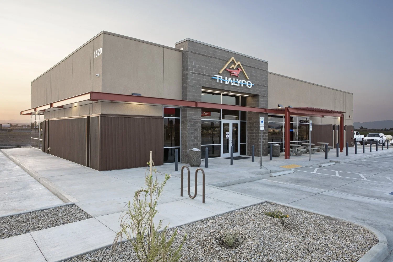 Exterior of a modern restaurant building with a sign that says 'THALYO' and a mountain logo, with a parking lot and picnic tables outside.