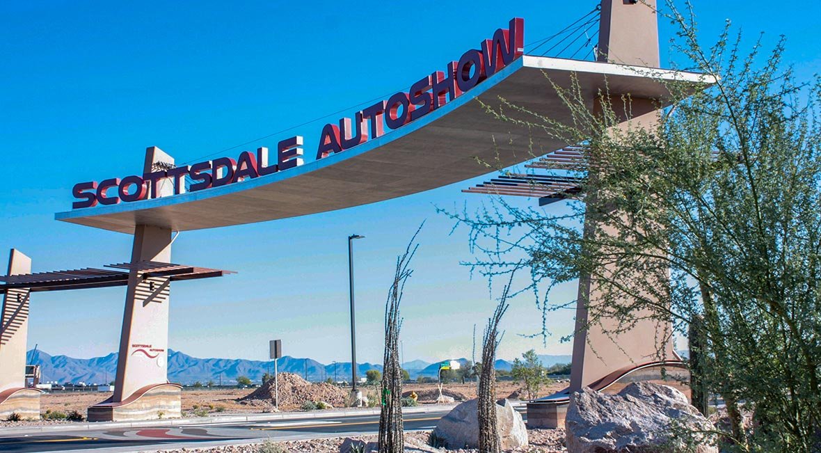 Entrance sign for Scottsdale Auto Show with mountains in the background and desert landscape with rocks and plants in the foreground.