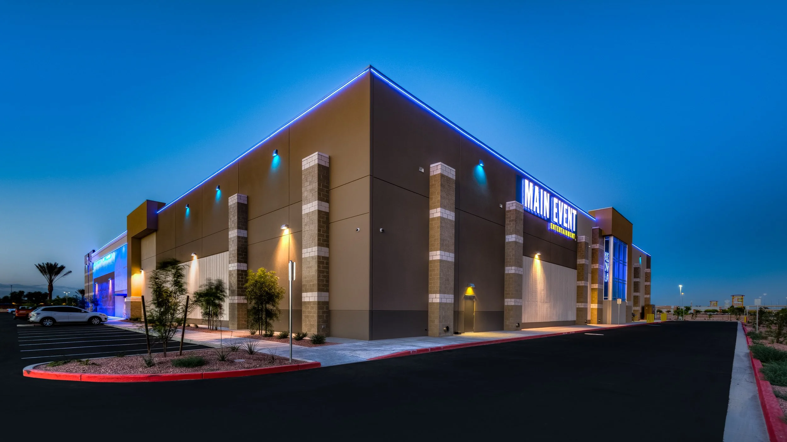 A modern commercial building with neon lights and parking lot at dusk.