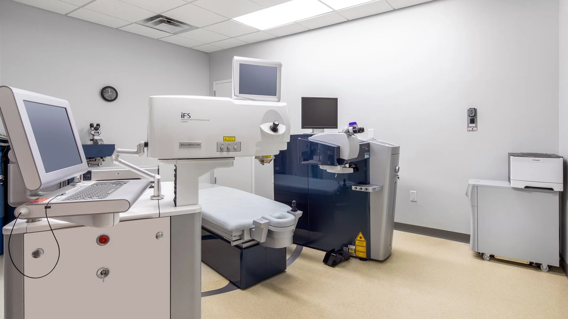 A medical room with specialized laser and diagnostic equipment, including a computer, monitor, and treatment bed.