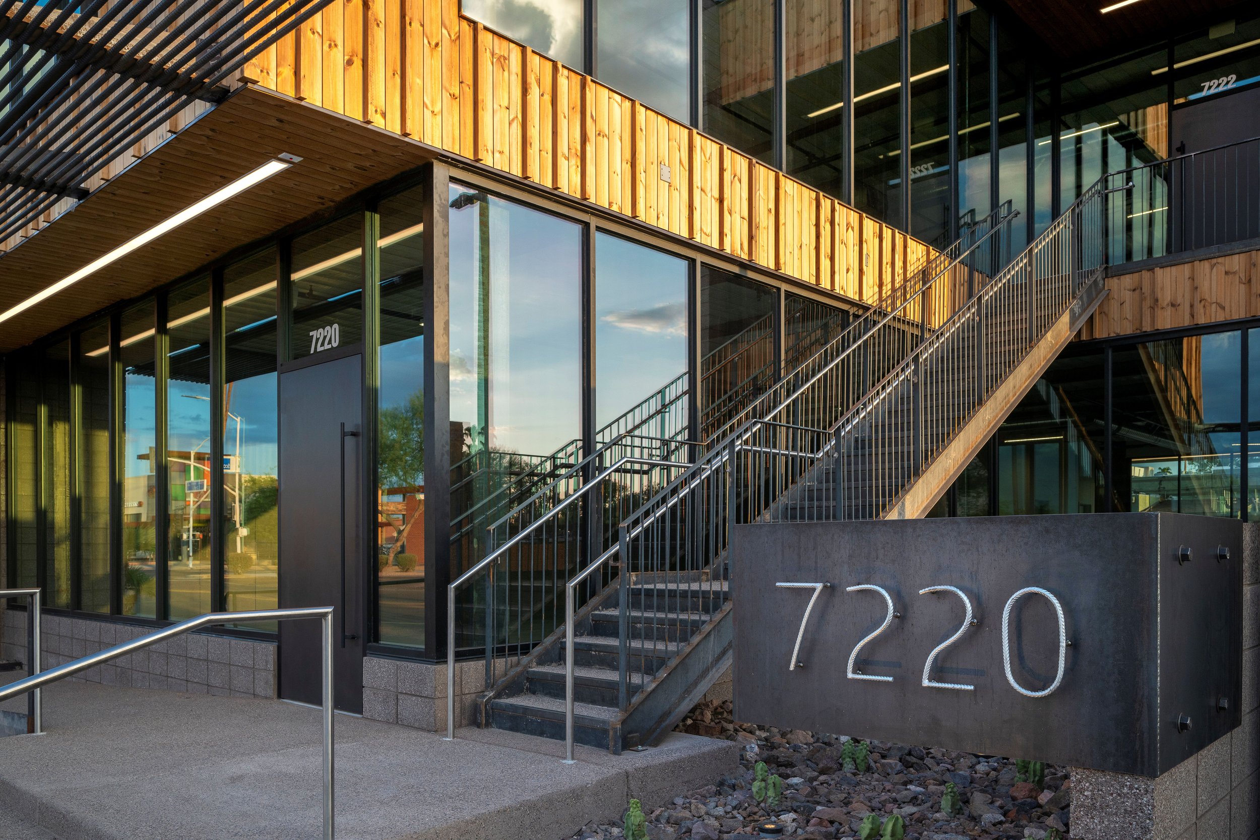 Modern building with large glass windows, wooden accents, metal stairs, and a sign displaying the street number 7220.
