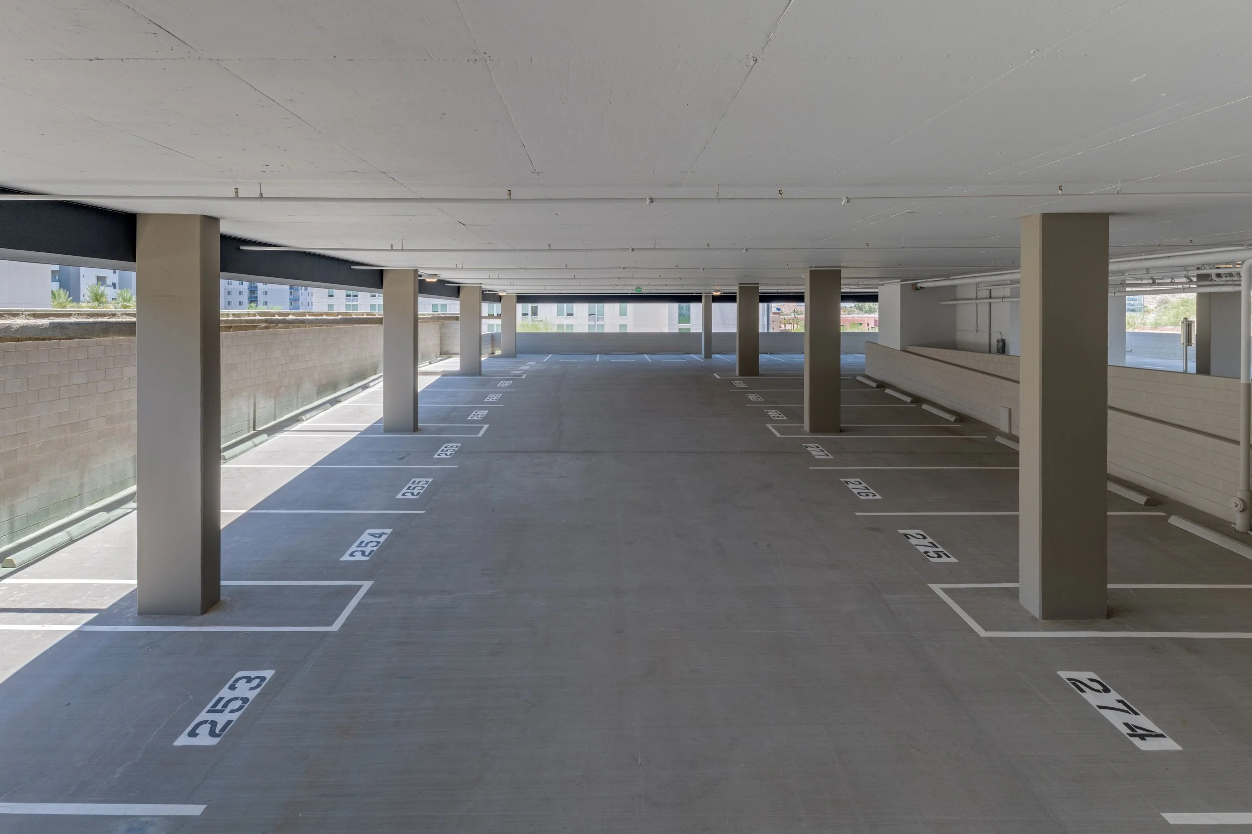 Empty multi-level parking garage with parked space numbers along the concrete floor and concrete support columns.