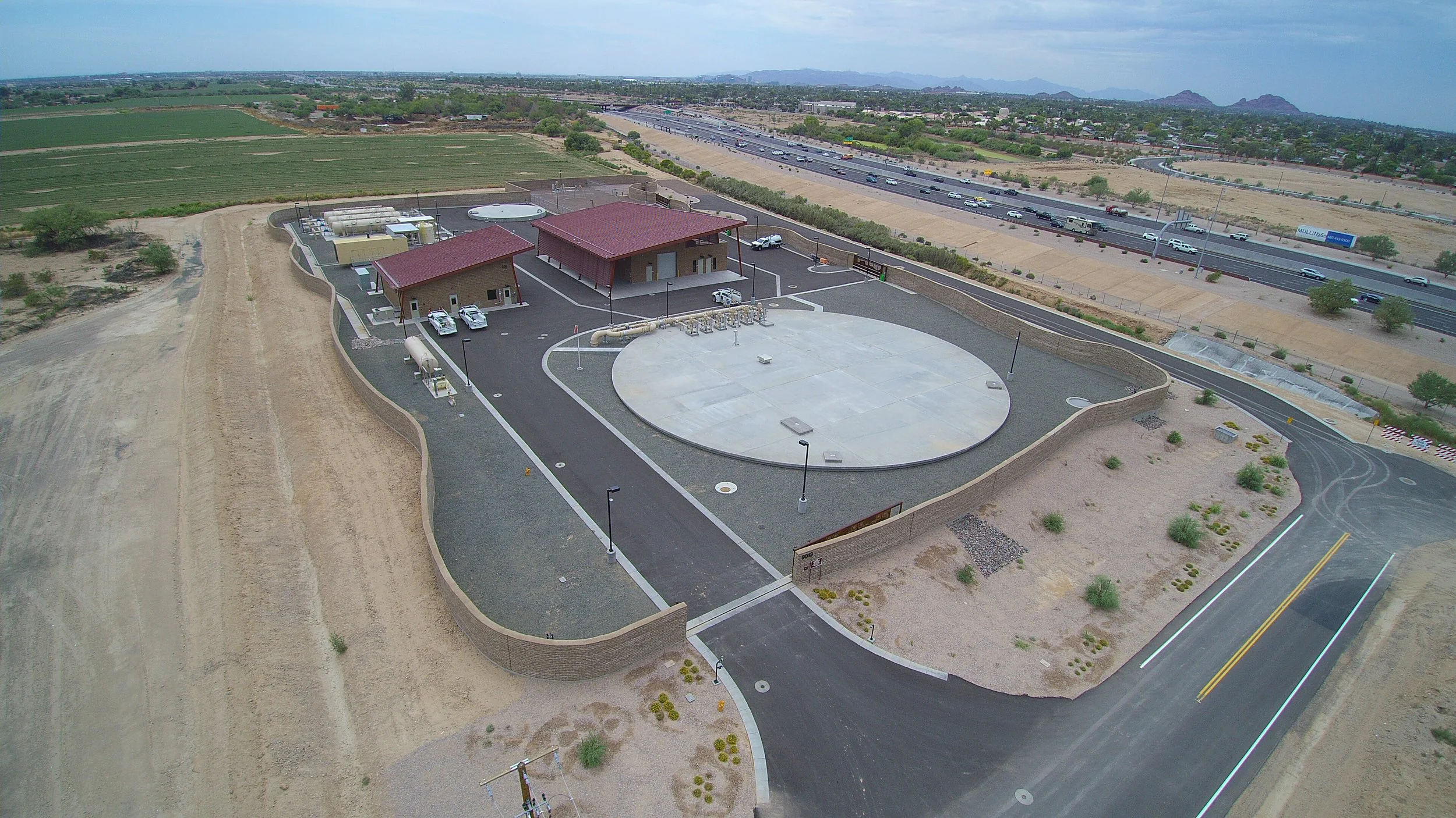 A small facility with a circular concrete pad, two buildings with red roofs, parking spaces, and surrounding desert landscape. A highway is visible in the background.
