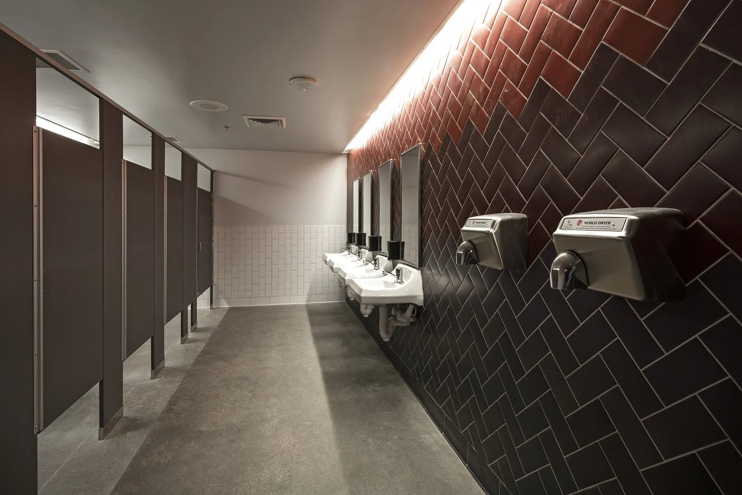 Public men's restroom with sinks, mirrors, and sliding stall doors.