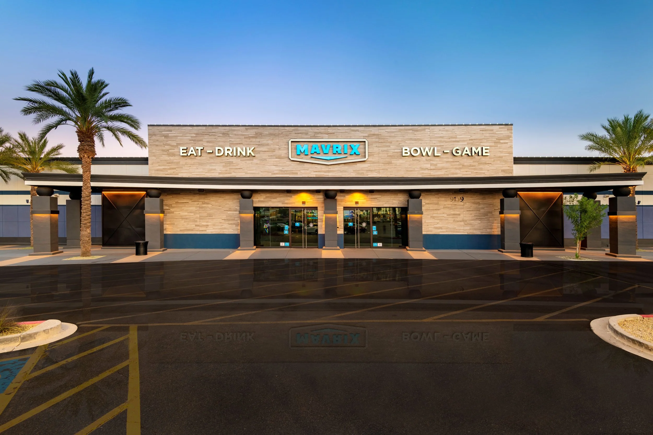 Exterior view of a Dave & Buster's entertainment restaurant with palm trees, parking lot, and a blue sky, displaying signs for eat-drink and bowl-game.