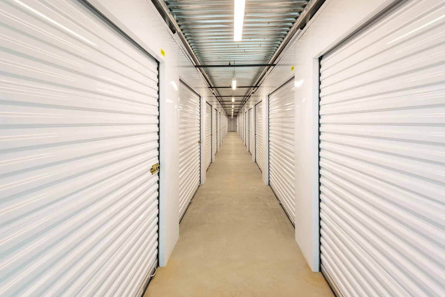 A hallway lined with closed white storage unit doors in a self-storage facility.