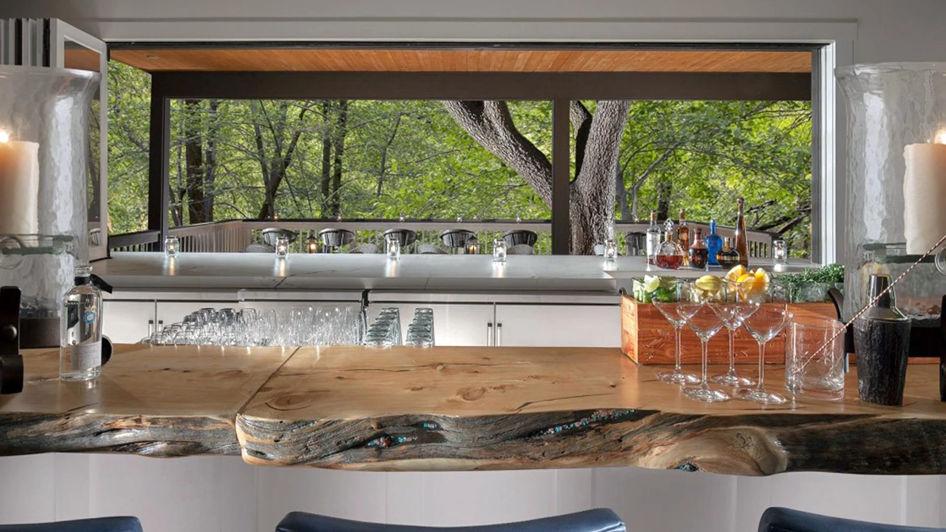 View from a bar counter looking out onto an outdoor deck with a large tree and green foliage visible through the window.