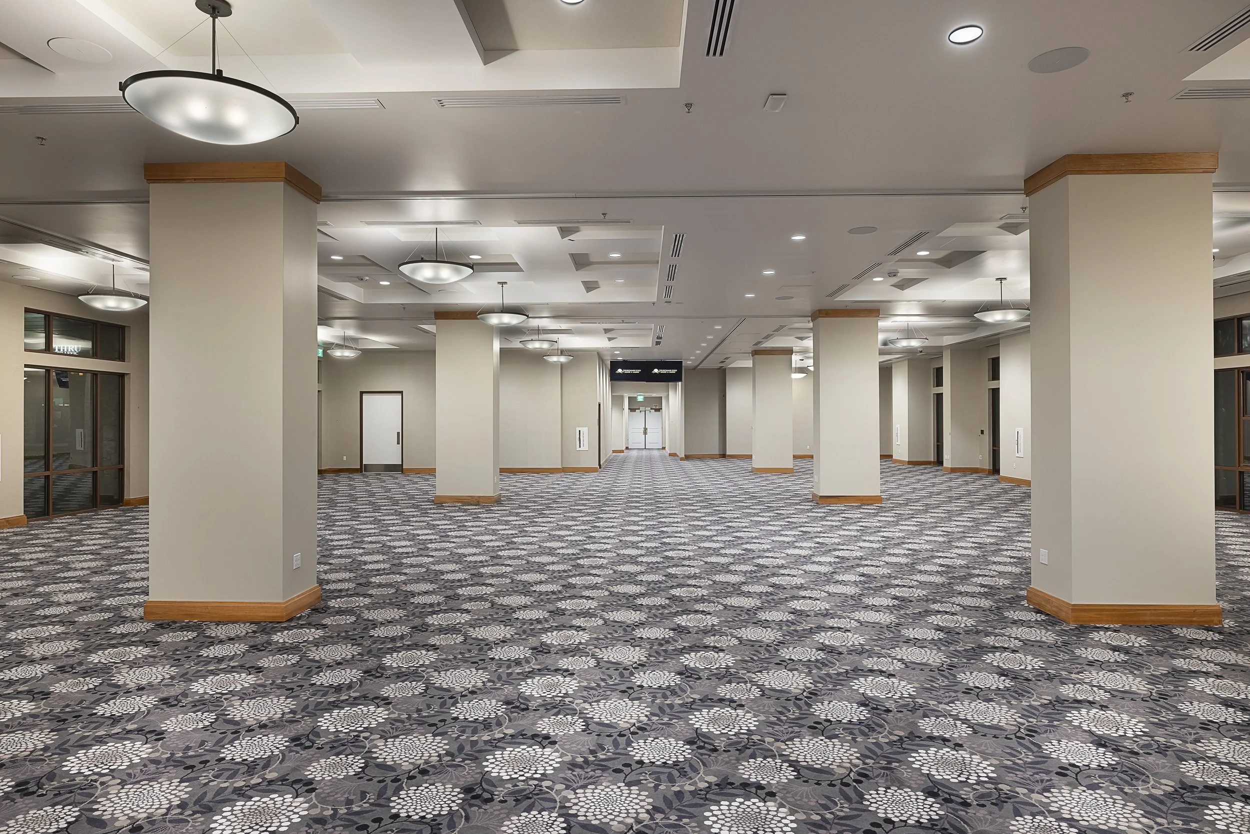 Empty conference or hotel lobby with patterned carpet, white walls, and ceiling lights.