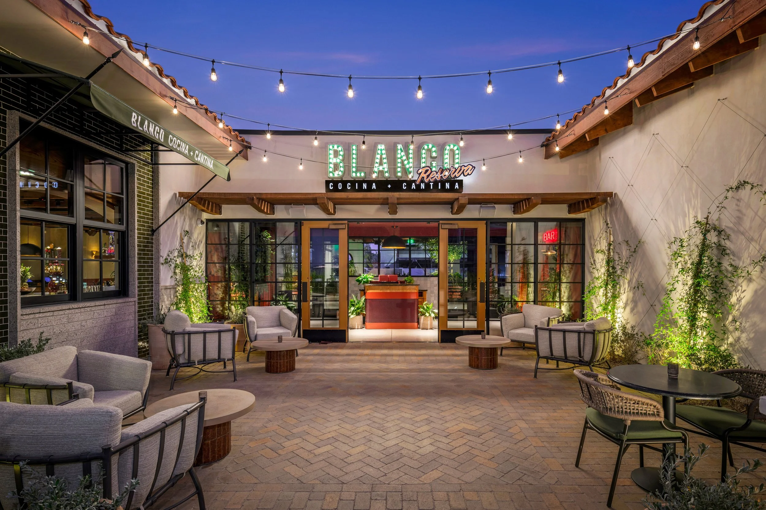Outdoor patio of a restaurant called Blanco Cocina + Cantina at dusk with string lights and patio furniture.