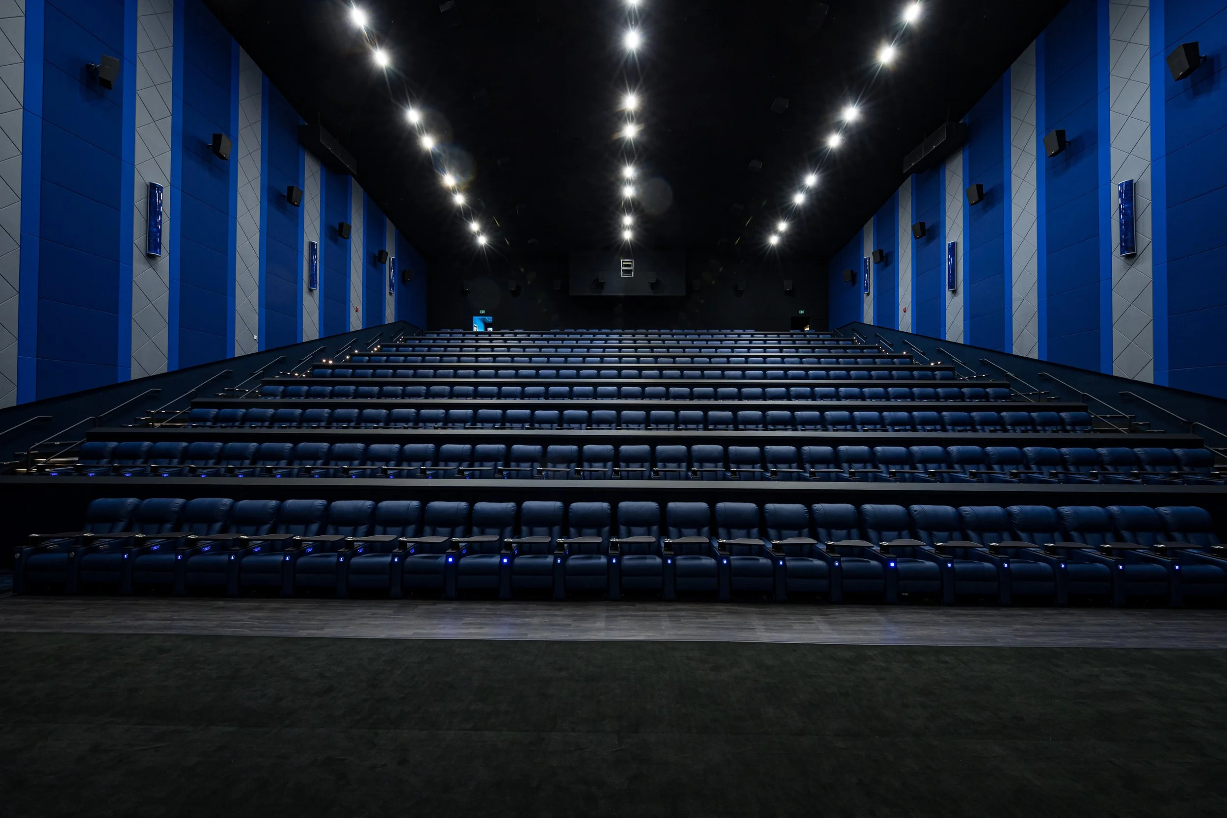 Empty movie theater with blue walls and rows of black leather seats, viewed from the front.