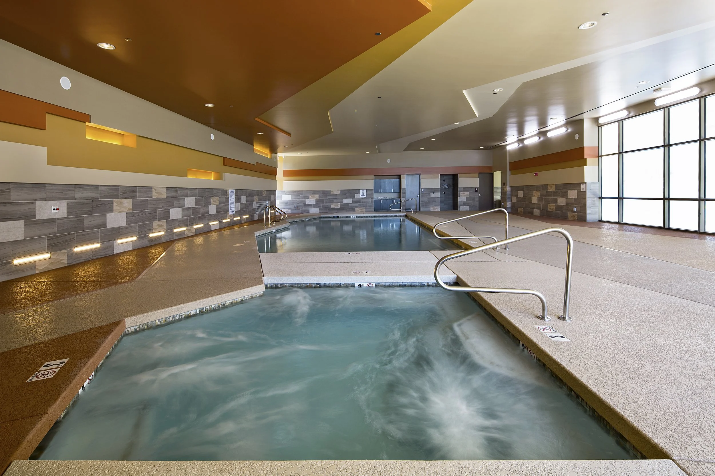 Indoor spa with hot tubs, beige flooring, and large windows allowing natural light.