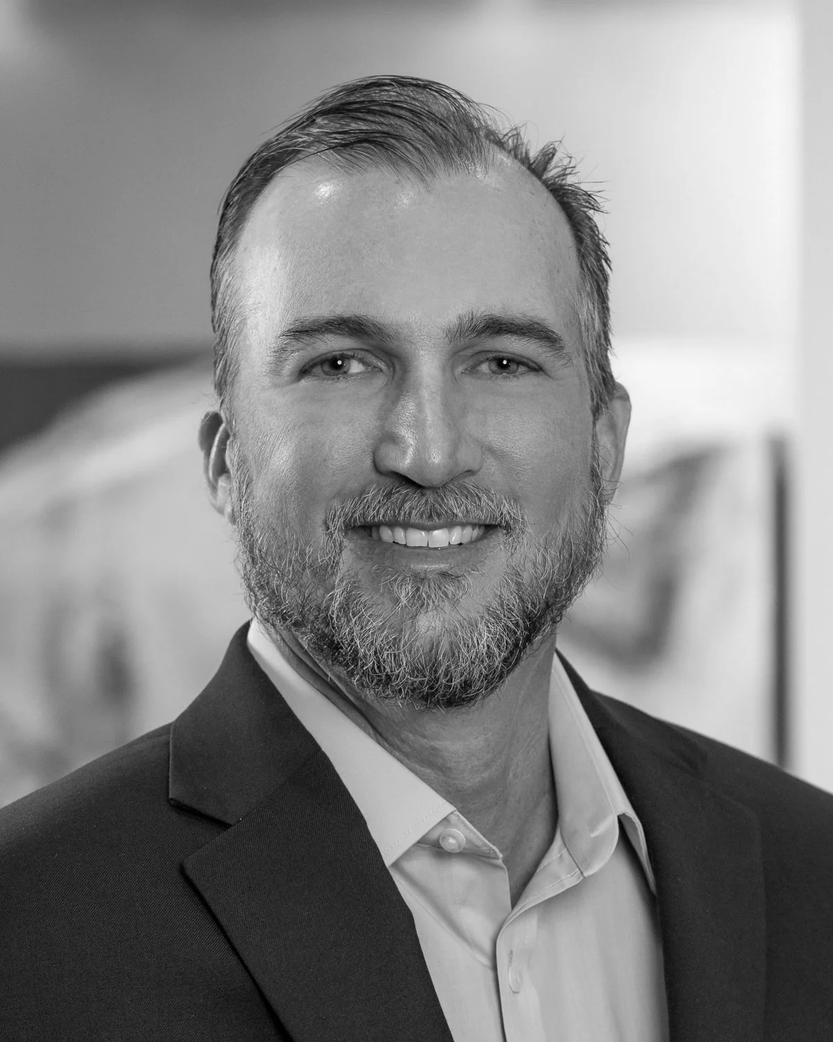 Black and white professional portrait Brian Reed, Vice President Preconstruction at A.R. Mays Construction, smiling and wearing a suit jacket and dress shirt.