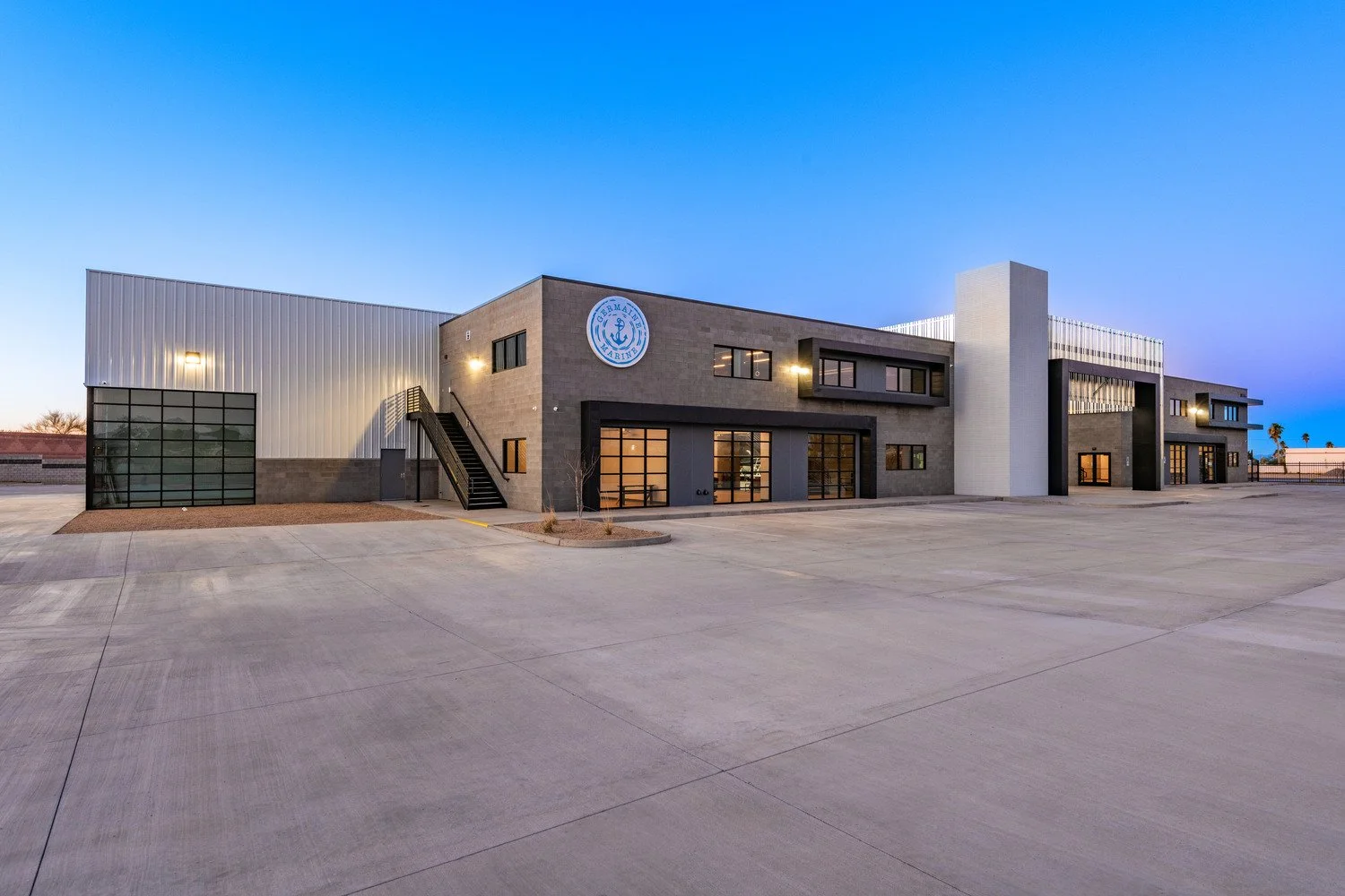 Modern building with a Marine Corps logo on the front, large glass doors, and a spacious parking area, during early evening with a clear sky.