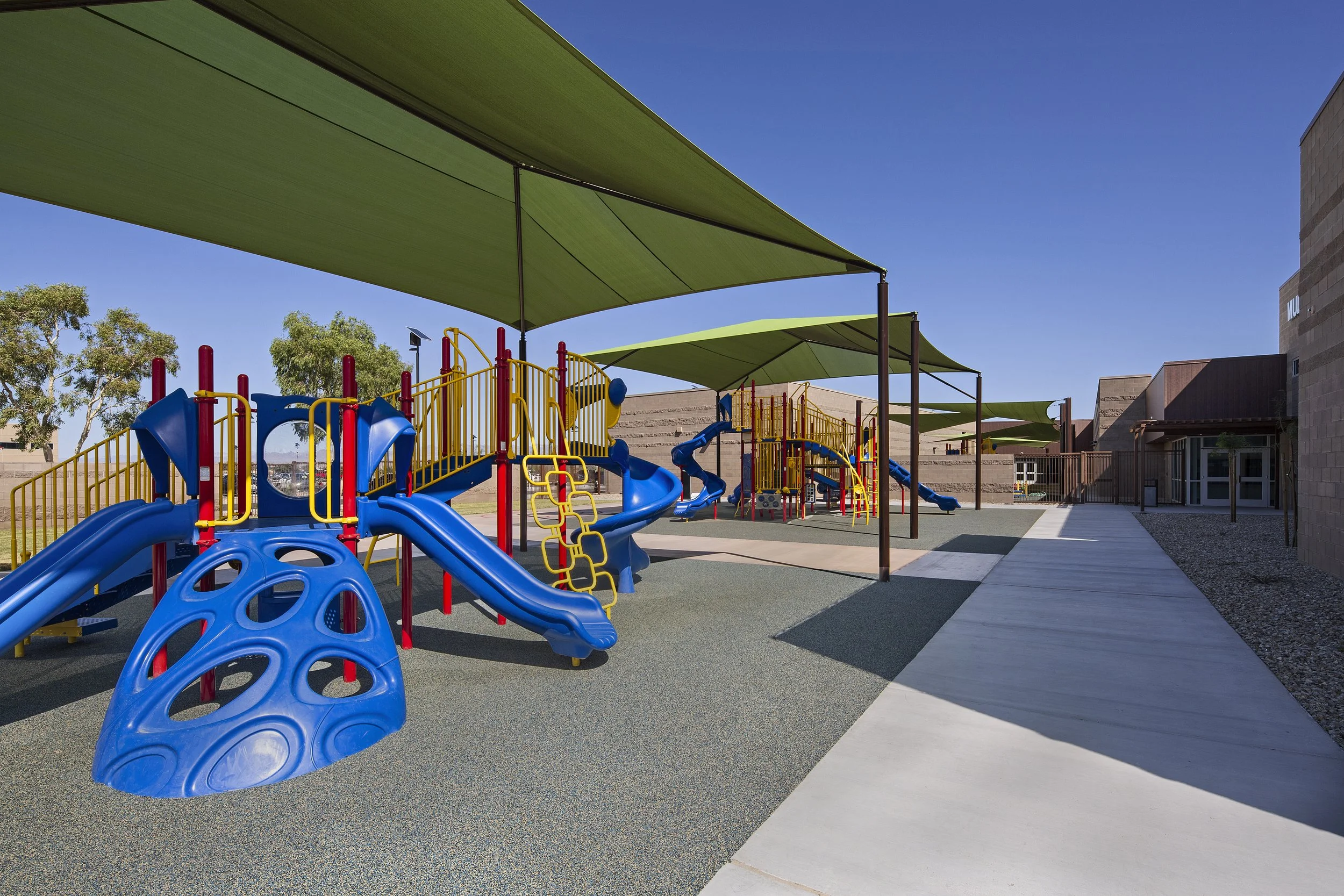 Colorful playground with blue slides, yellow climbing structures, and shaded green canopies on a sunny day.