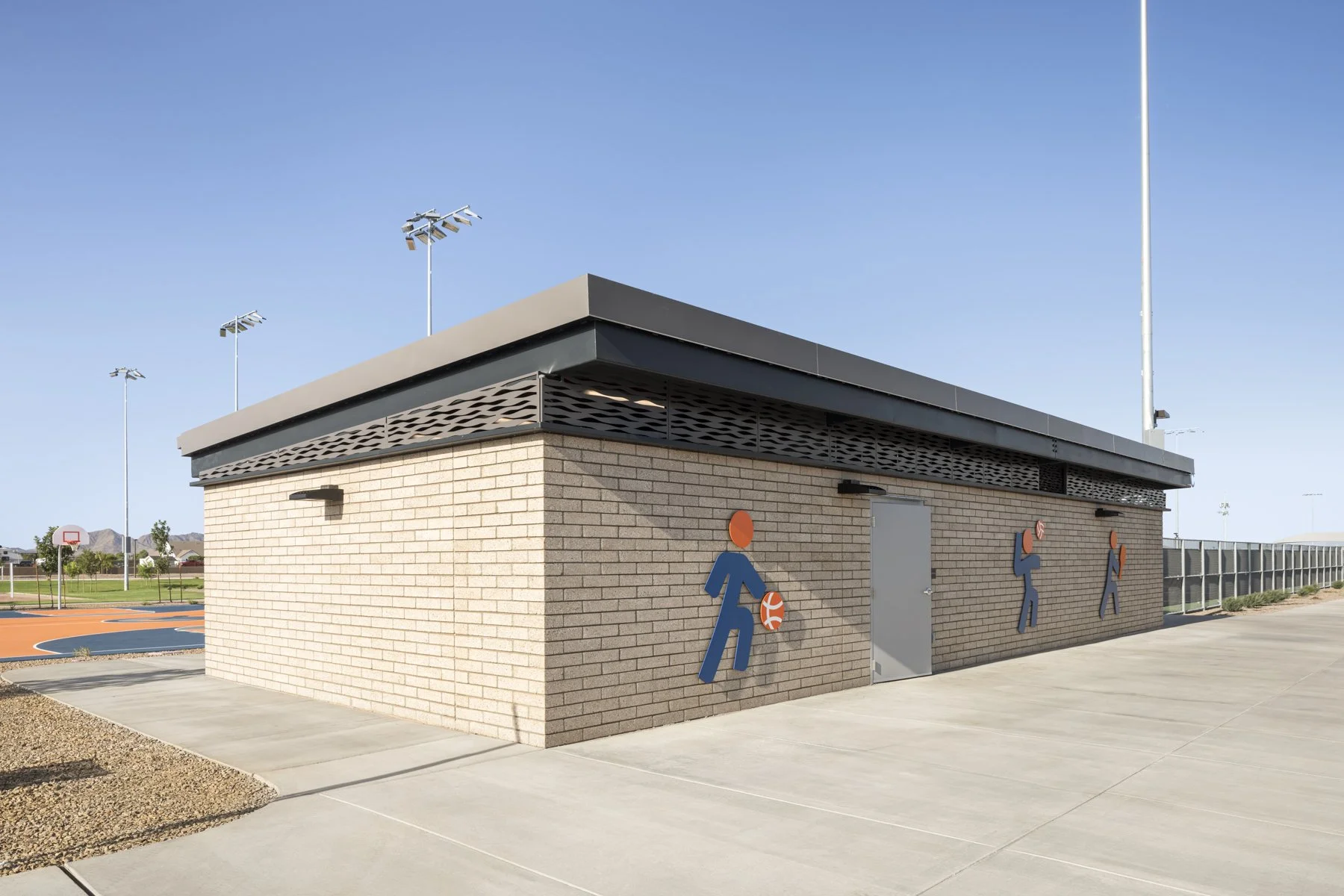 Side of a brick sports facility with three nautical-themed icons and a basketball court in the background.