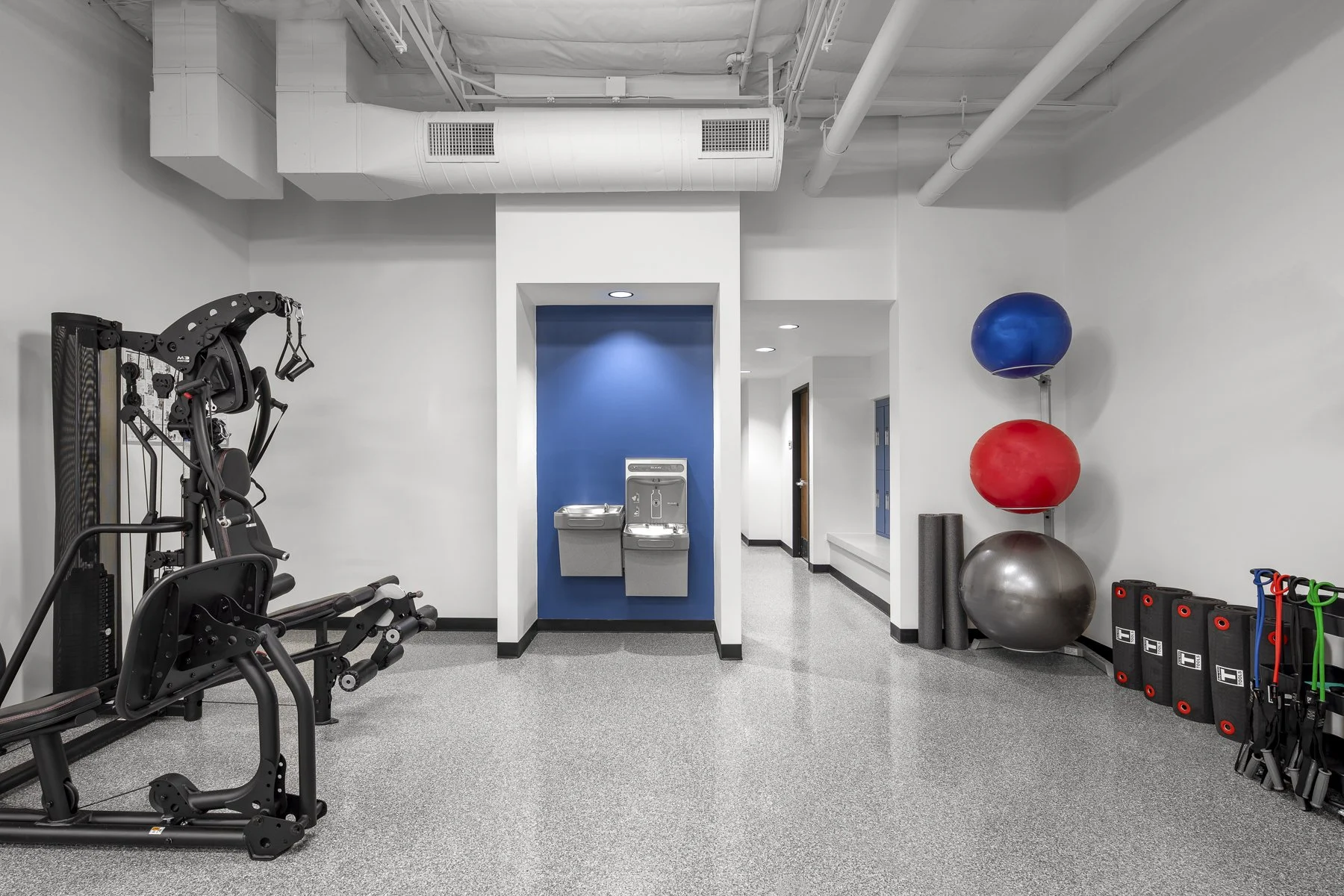 Empty modern gym with strength and balance equipment, water fountain, and blue, red, and silver exercise balls.