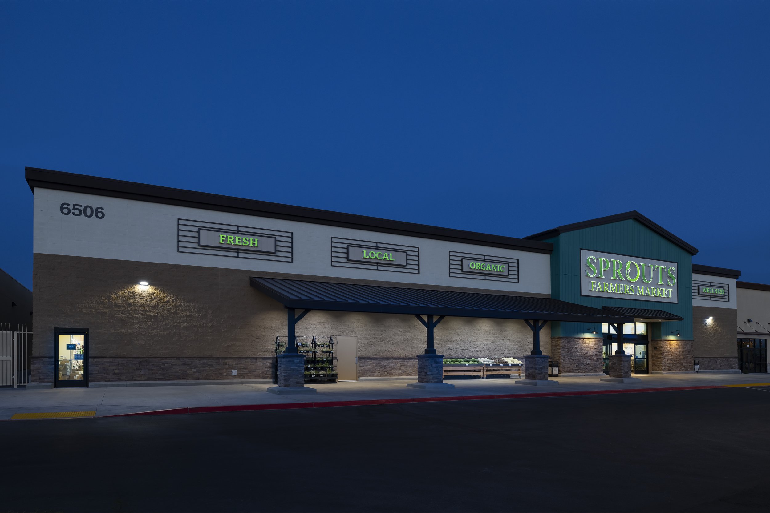 Exterior view of Sprouts Farmers Market store at night with illuminated green signs and a dark blue sky.