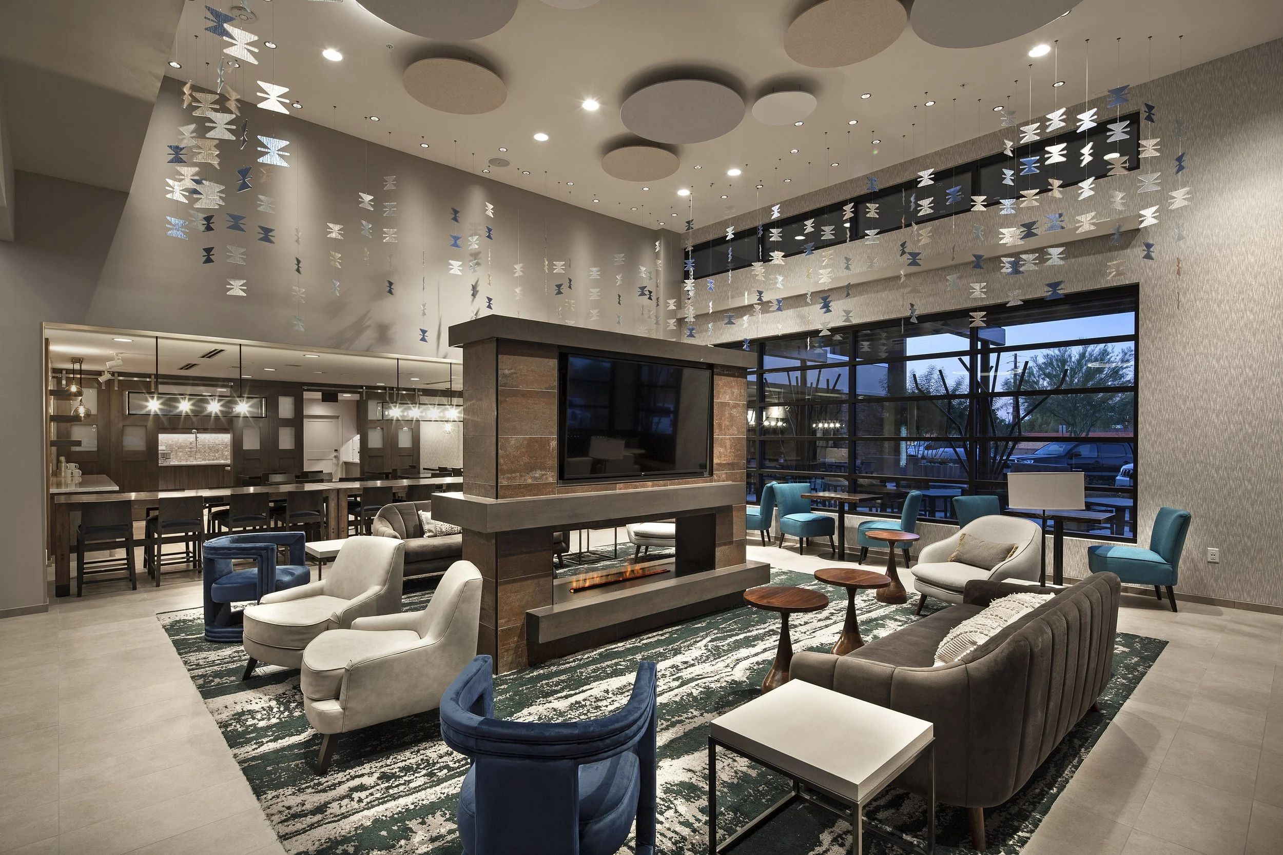 A modern hotel lobby with seating area, a fireplace, large window, and ceiling decorations.