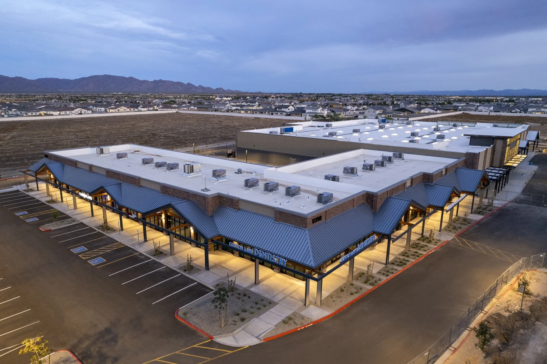 Aerial view of a modern commercial building with parking lot, featuring a dental office, located in a suburban area with mountains in the background.