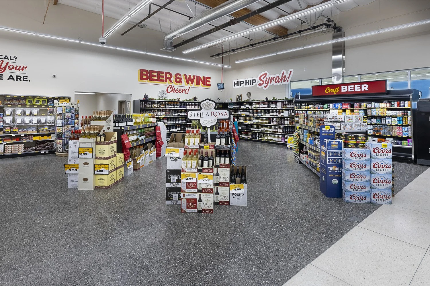 Interior of a liquor store with shelves stocked with beer and wine, and signage promoting beer and wine, with the brand Stella Rosa prominently displayed in the center.
