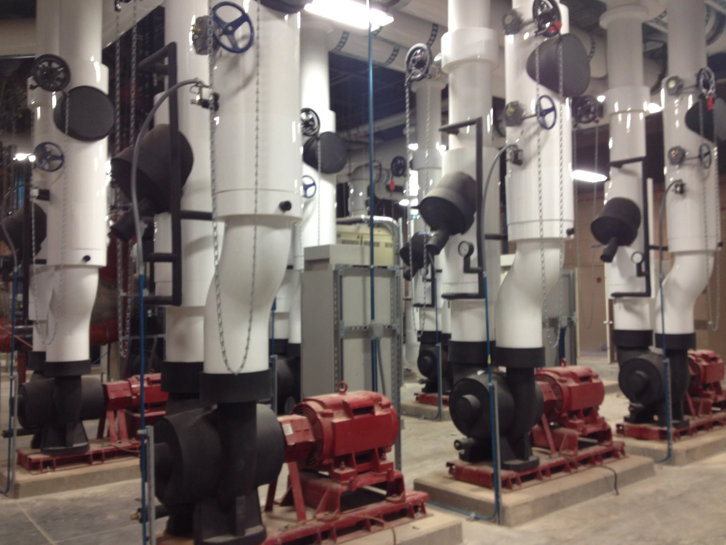 Industrial equipment with white pipes, black valves, and red supports in a factory or mechanical room.