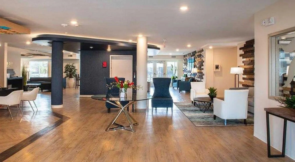 Lobby with seating area, plants, and wooden accents near large windows.